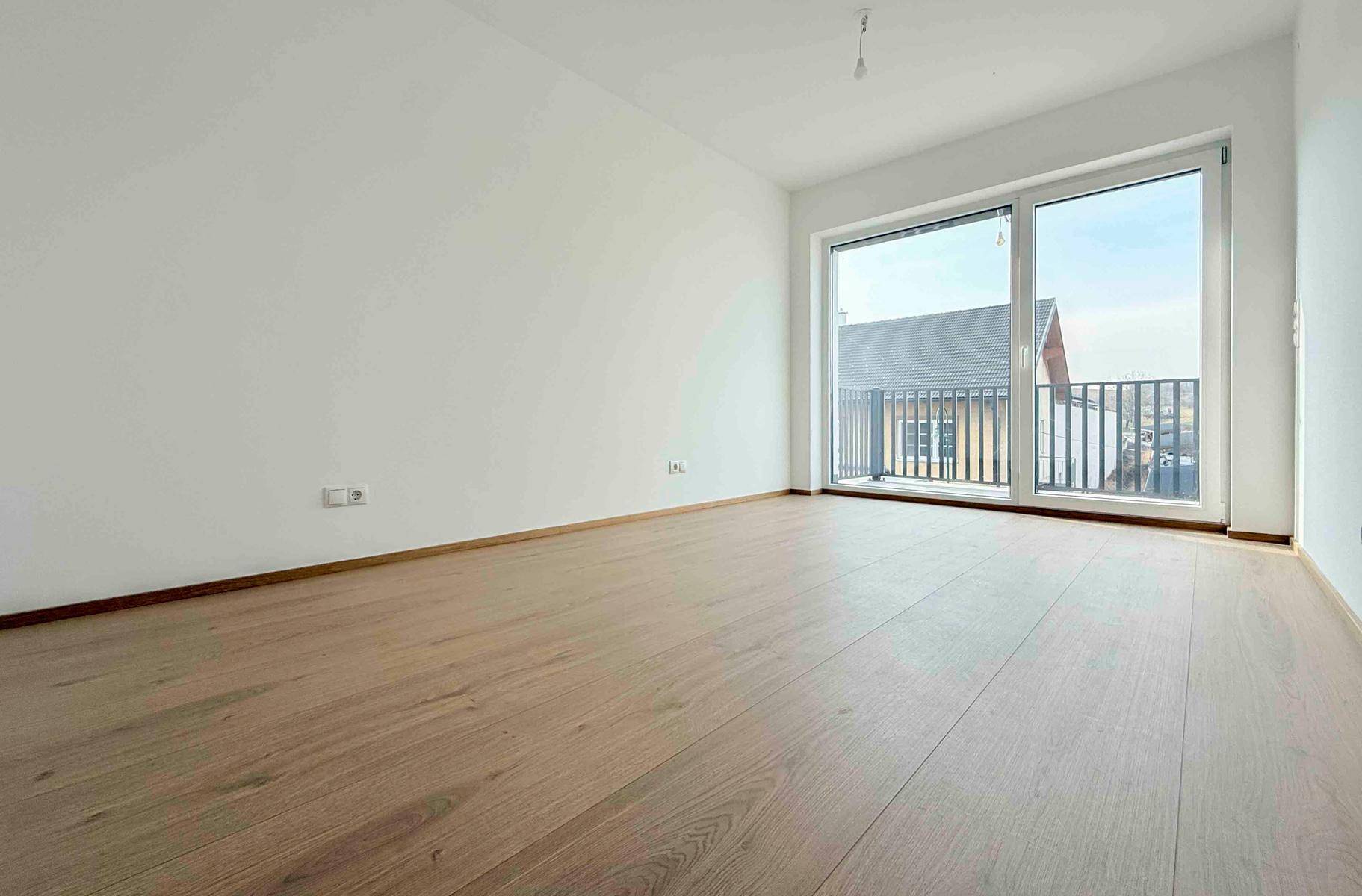 Heller, leerer Raum mit Laminatboden und großer Fensterfront, die einen weiten Blick ermöglicht.