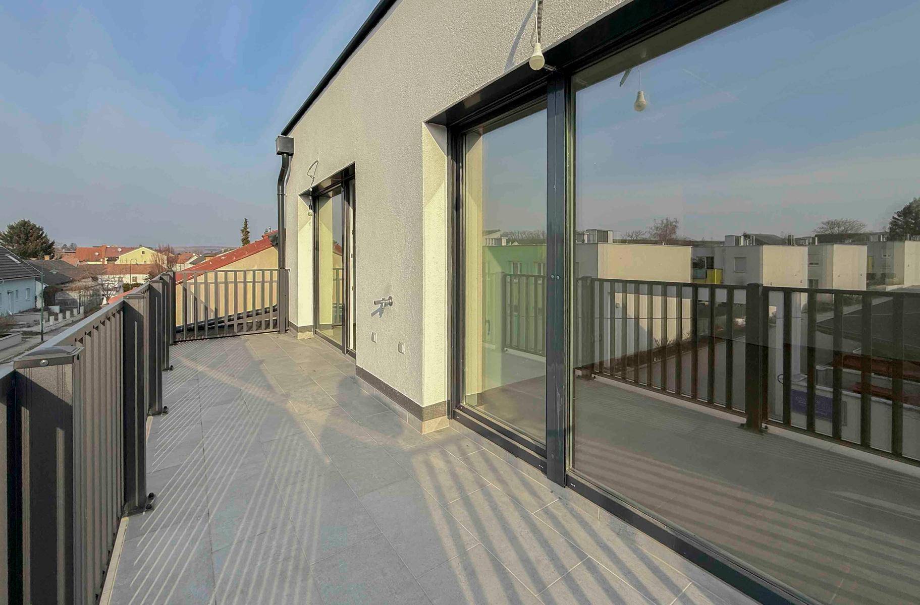 Großzügige Terrasse mit Fliesenboden und modernem Geländer, bietet einen weiten Ausblick.