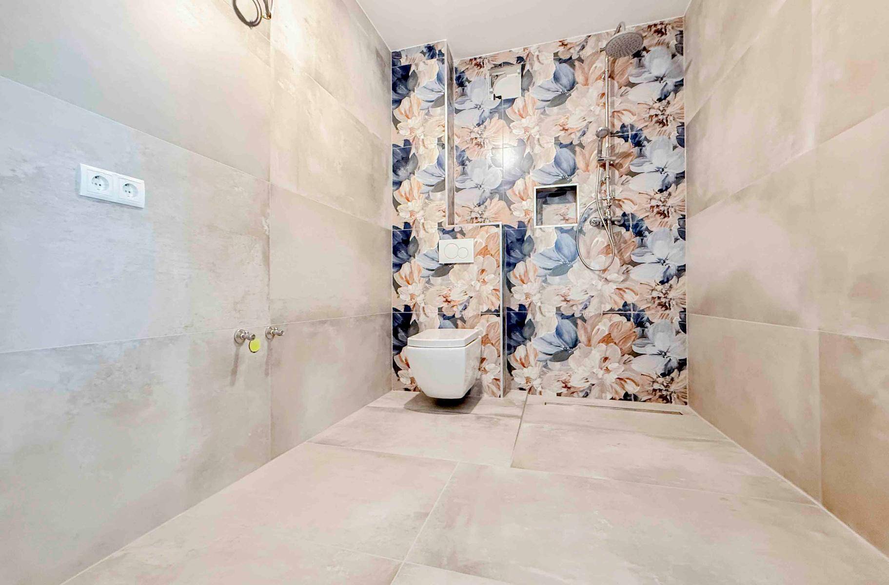 Modernes Badezimmer mit wandhängendem WC und Duschbereich, akzentuiert durch farbenfrohe Wandfliesen.