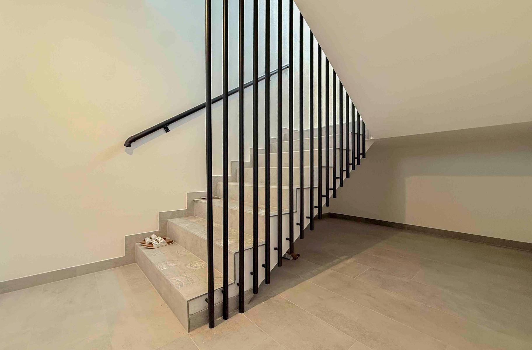 Moderne Treppe mit schwarzem vertikalen Geländer und Fliesenstufen, verbindet die Stockwerke.