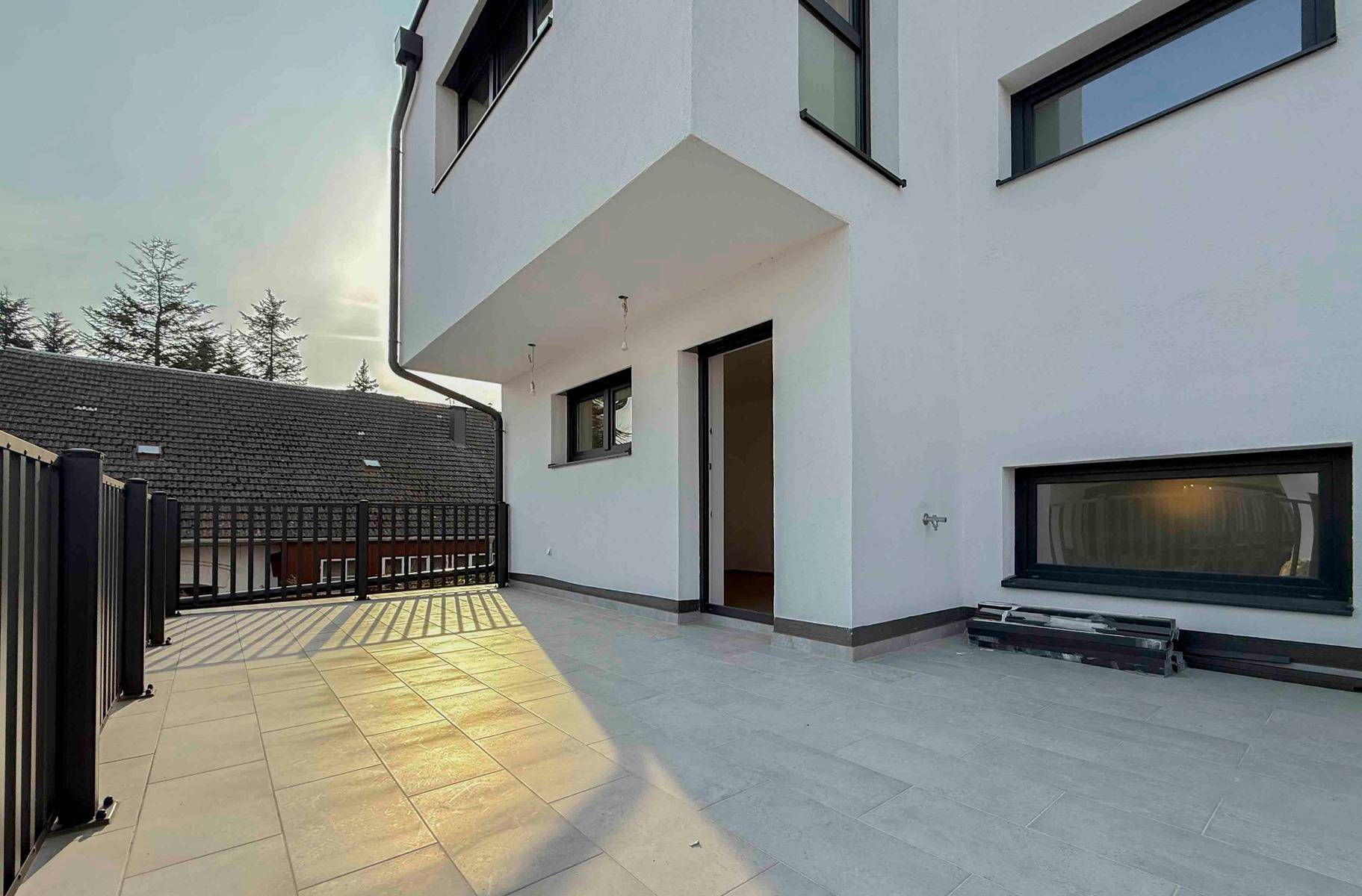 Geräumige Terrasse mit Fliesenboden und modernem Geländer, bietet einen weiten Blick auf die Umgebung.