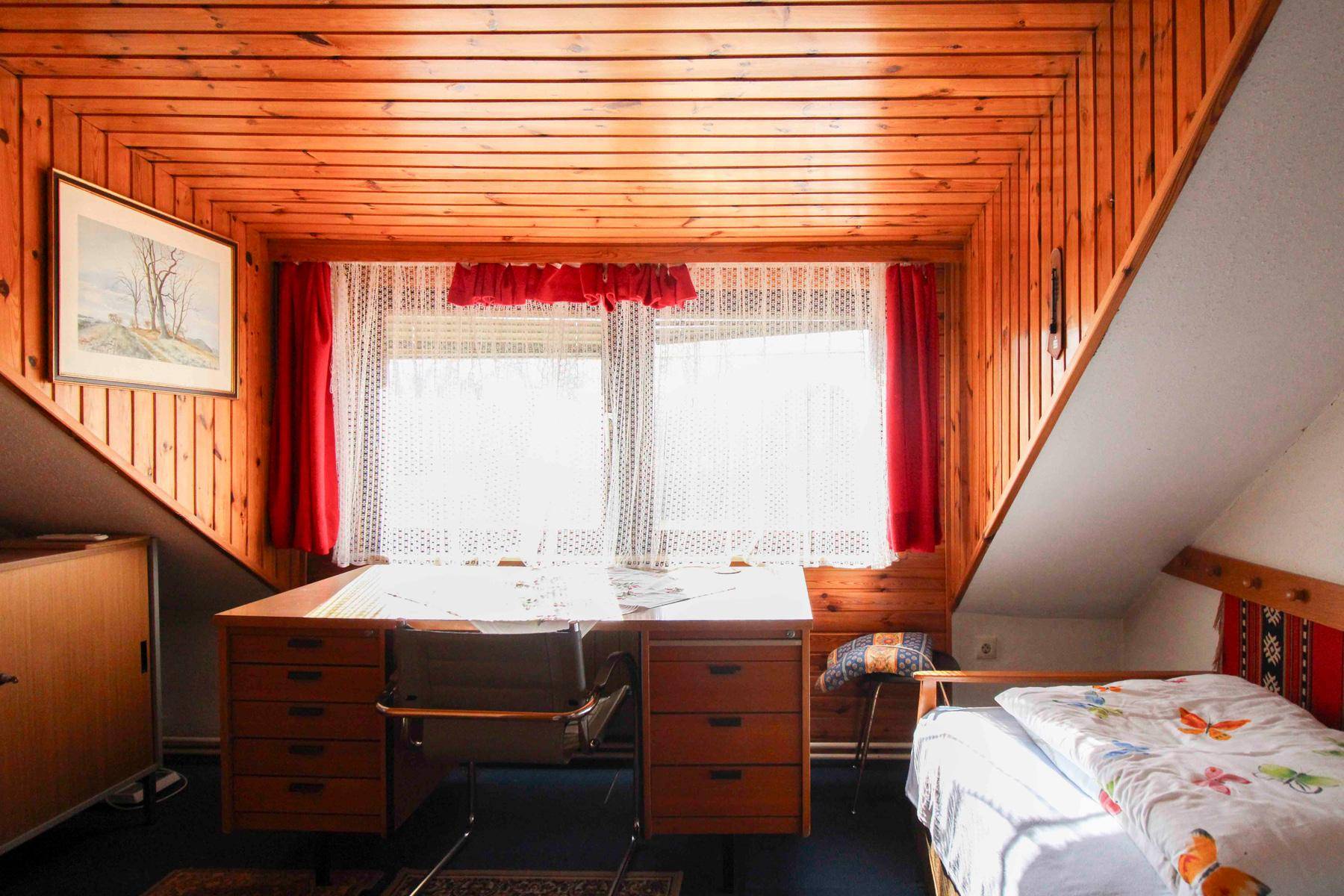 Helles Dachgeschosszimmer mit Holzverkleidung, Schreibtisch und Dachschräge.