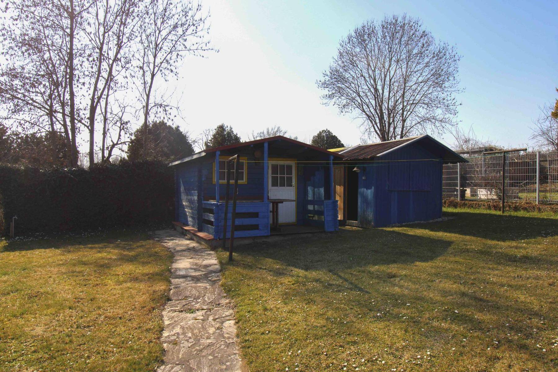 Blau gestrichene Gartenhütte mit kleinem Vordach und umgebender Rasenfläche.