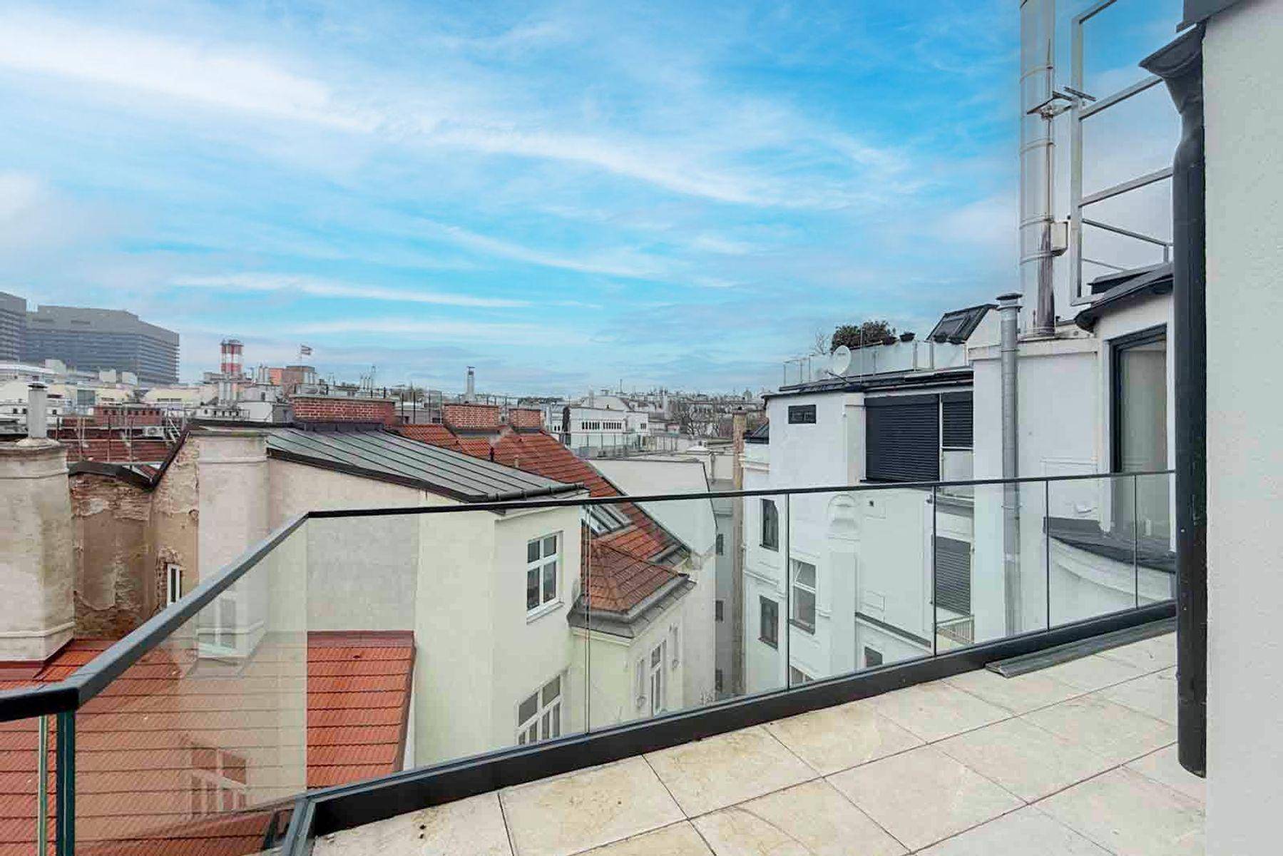 Geräumige Dachterrasse mit Glasgeländer und weitem Blick über die Dächer der Stadt.