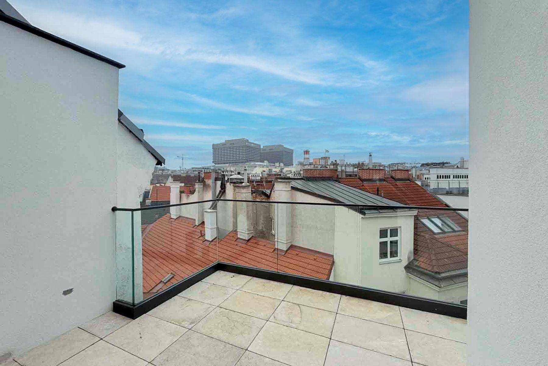 Helle Dachterrasse mit Fliesenboden und Glasgeländer, bietet einen weiten Stadtblick.