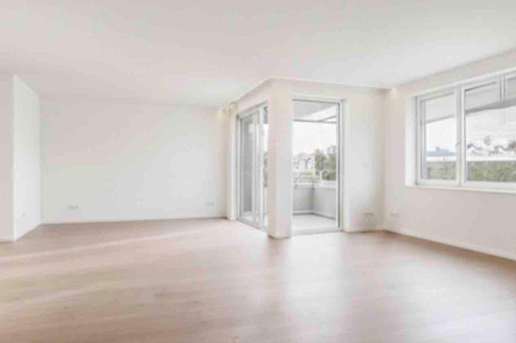 Heller, leerer Wohnbereich mit Holzboden und Zugang zu einem kleinen Balkon.