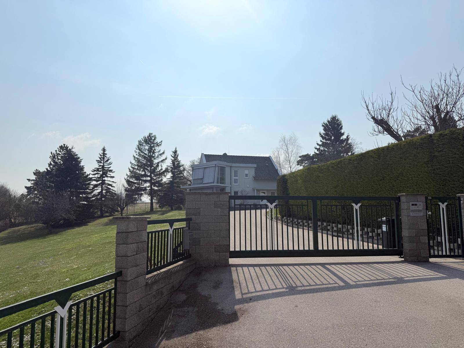Einfahrtstor zum Anwesen mit Blick auf das moderne Haus und die umliegende grüne Landschaft.