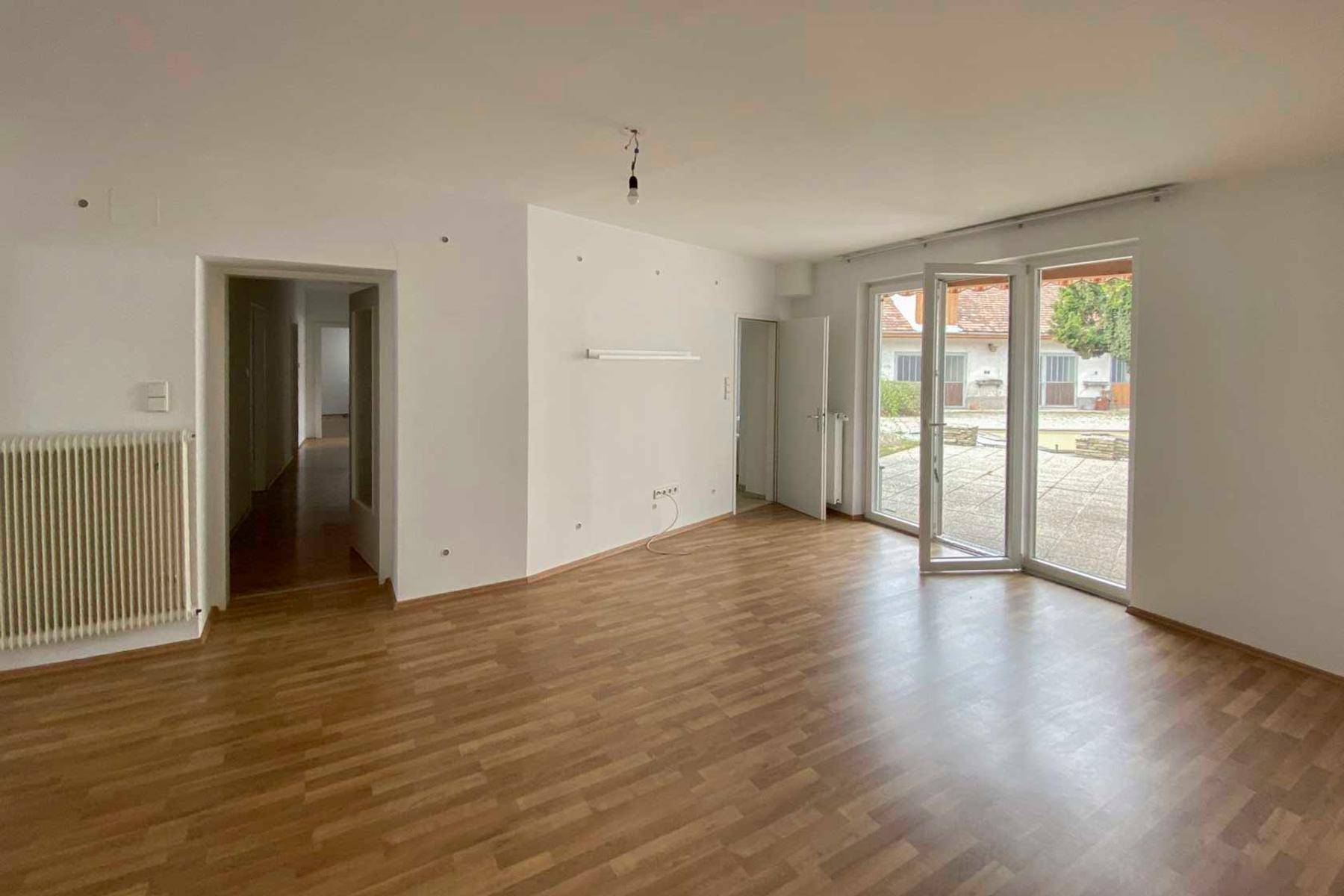 Geräumiges Wohnzimmer mit Parkettboden und großen Fenstertüren, die zum Außenbereich führen.