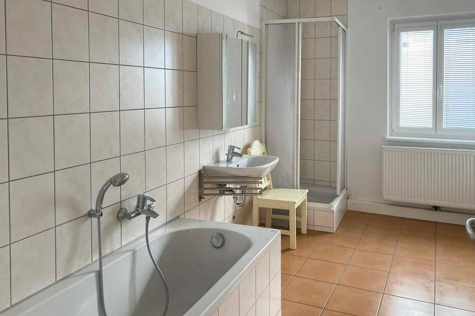 Badezimmer mit Badewanne, Duschkabine, Waschbecken und einem Fenster für natürliche Belüftung.