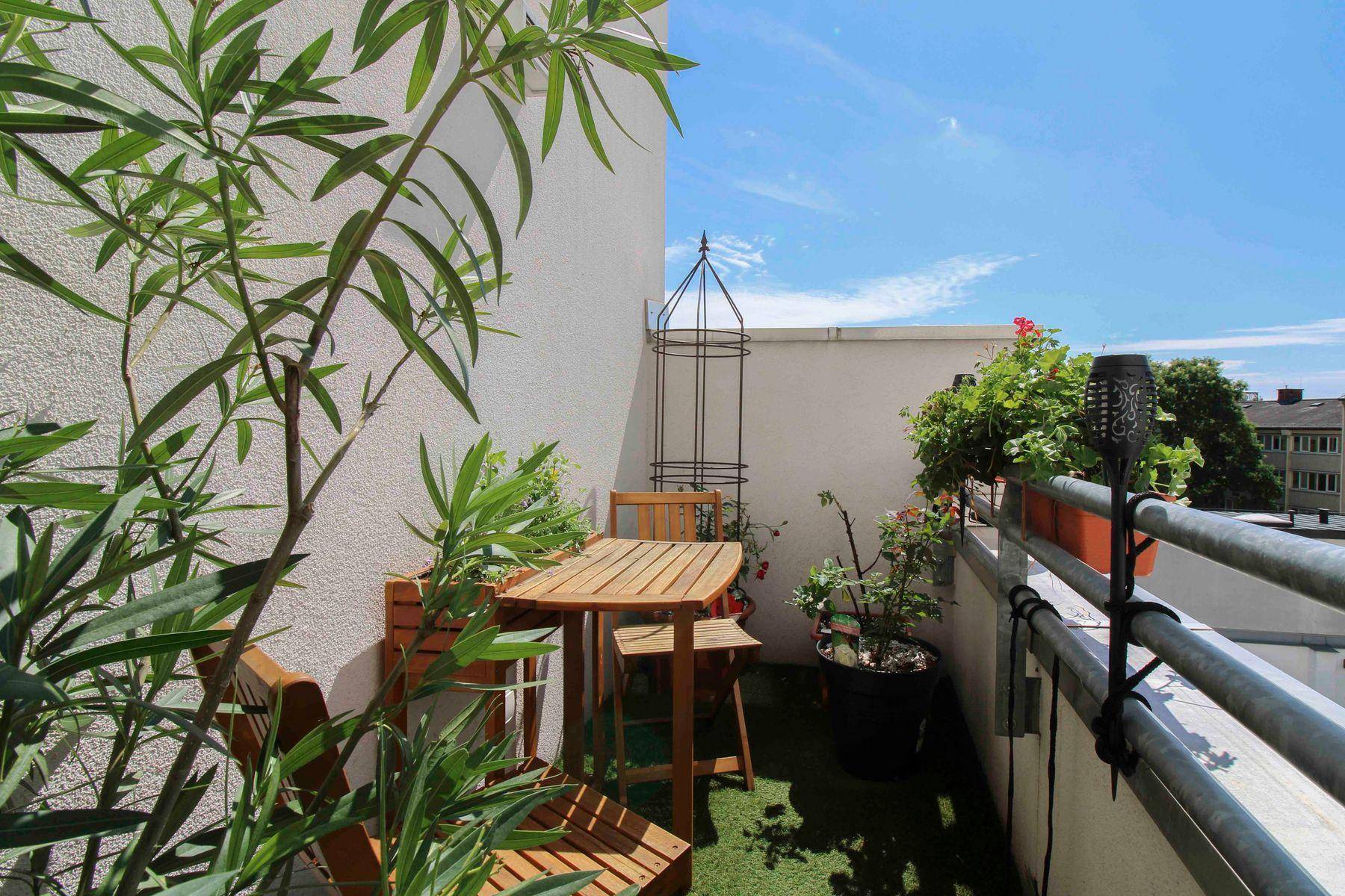 Kleiner, begrünter Balkon mit Holztisch und Stühlen, ideal für entspannte Stunden.