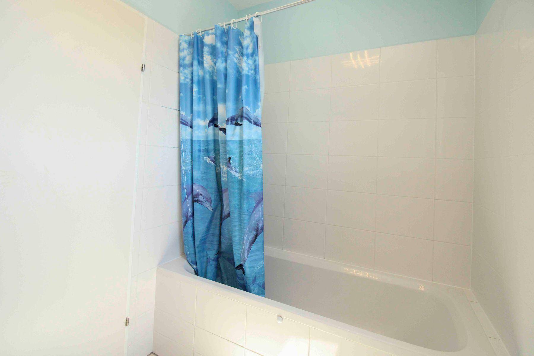 Badezimmer mit Badewanne und farbenfrohem Duschvorhang, umgeben von weißen Fliesen.