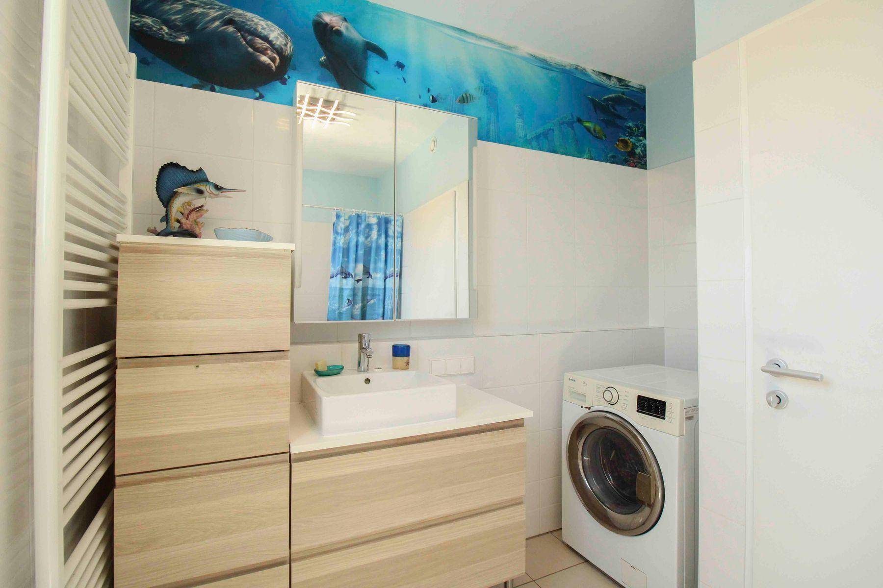 Badezimmer mit Waschbecken, Spiegelschrank, Waschmaschine und verspielter Wanddekoration.