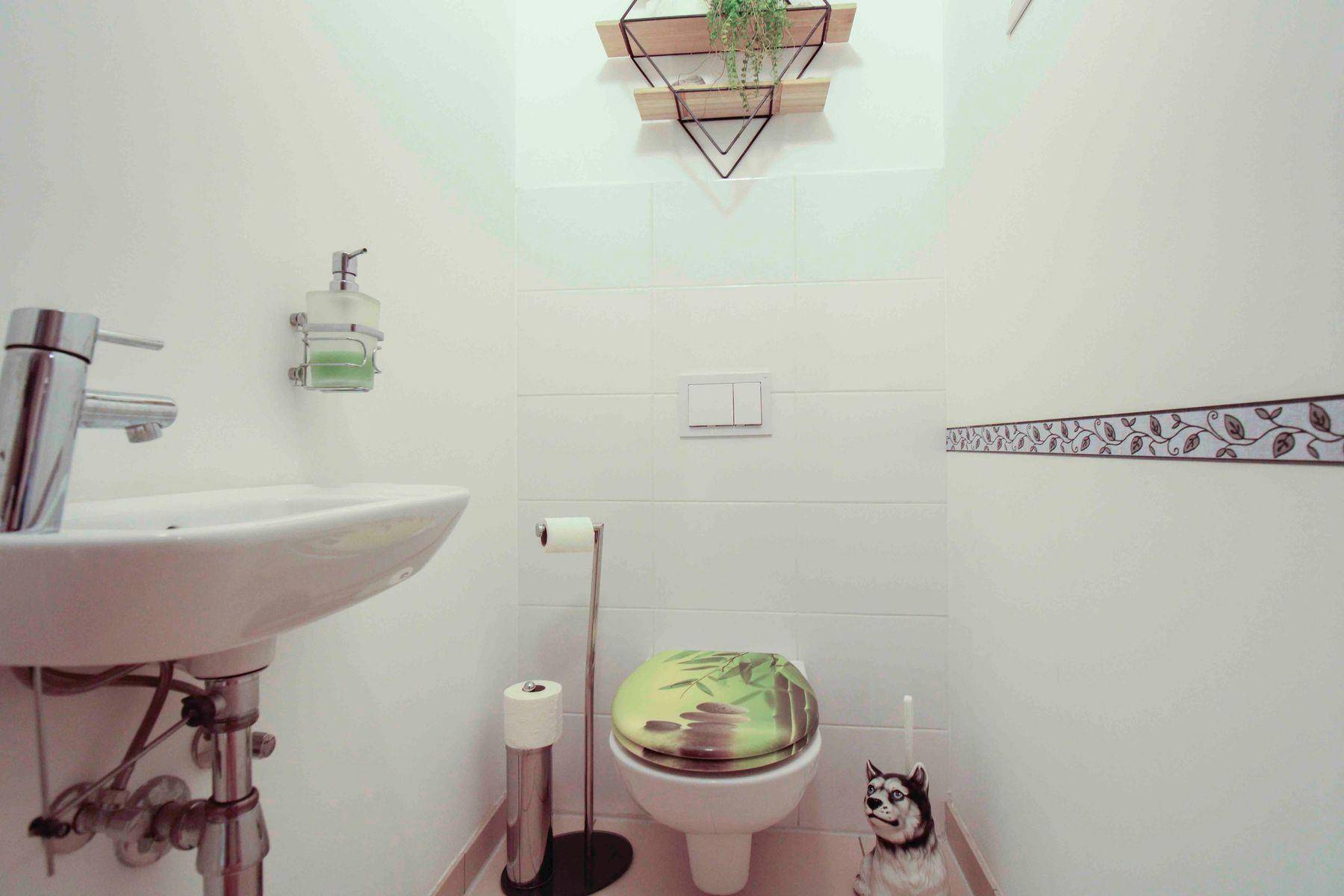 Gäste-WC mit Waschbecken, Toilette und dekorativer Bordüre an der Wand.