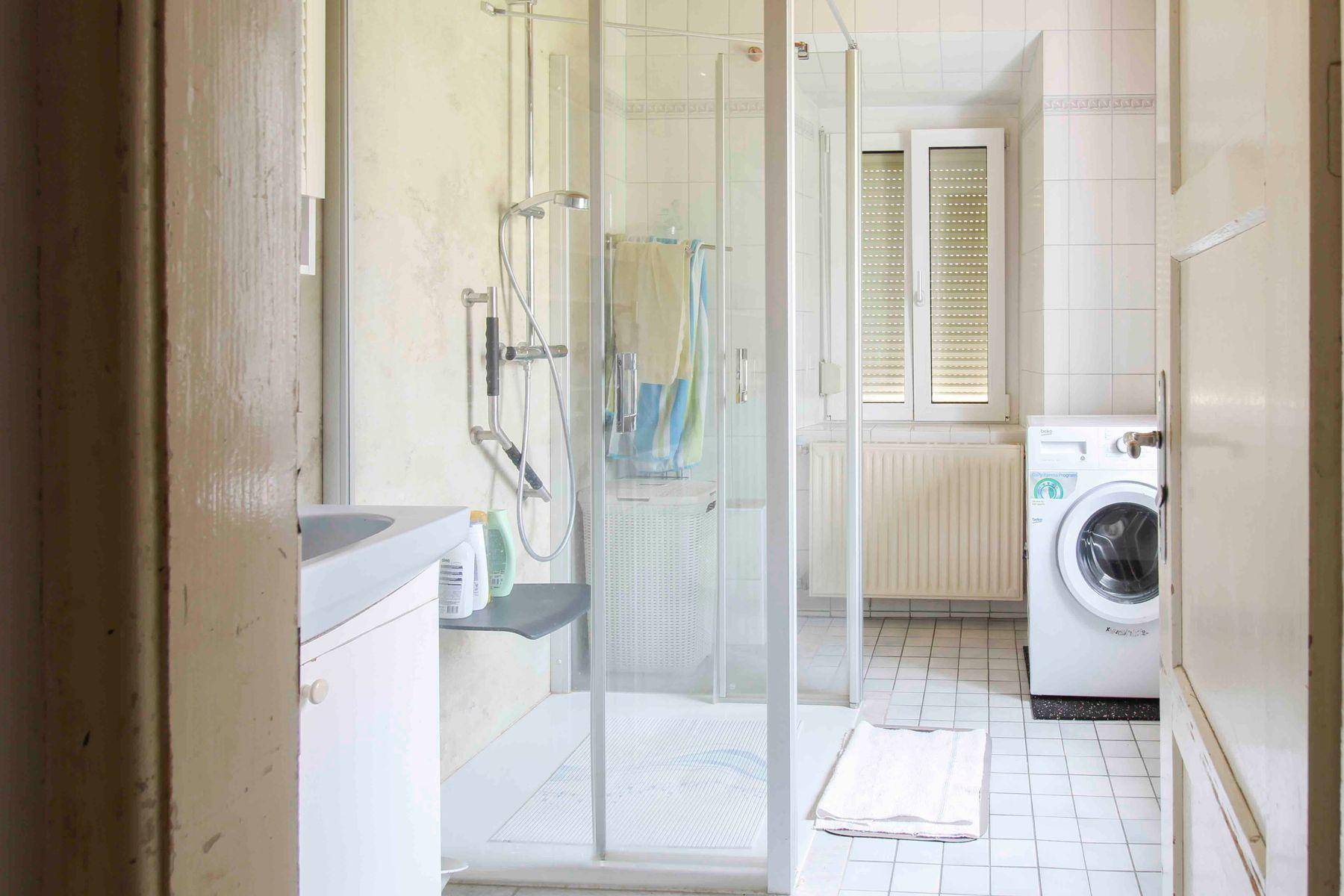 Helles Badezimmer mit Duschkabine, Waschmaschine und weißen Fliesen, funktional und gut gepflegt.