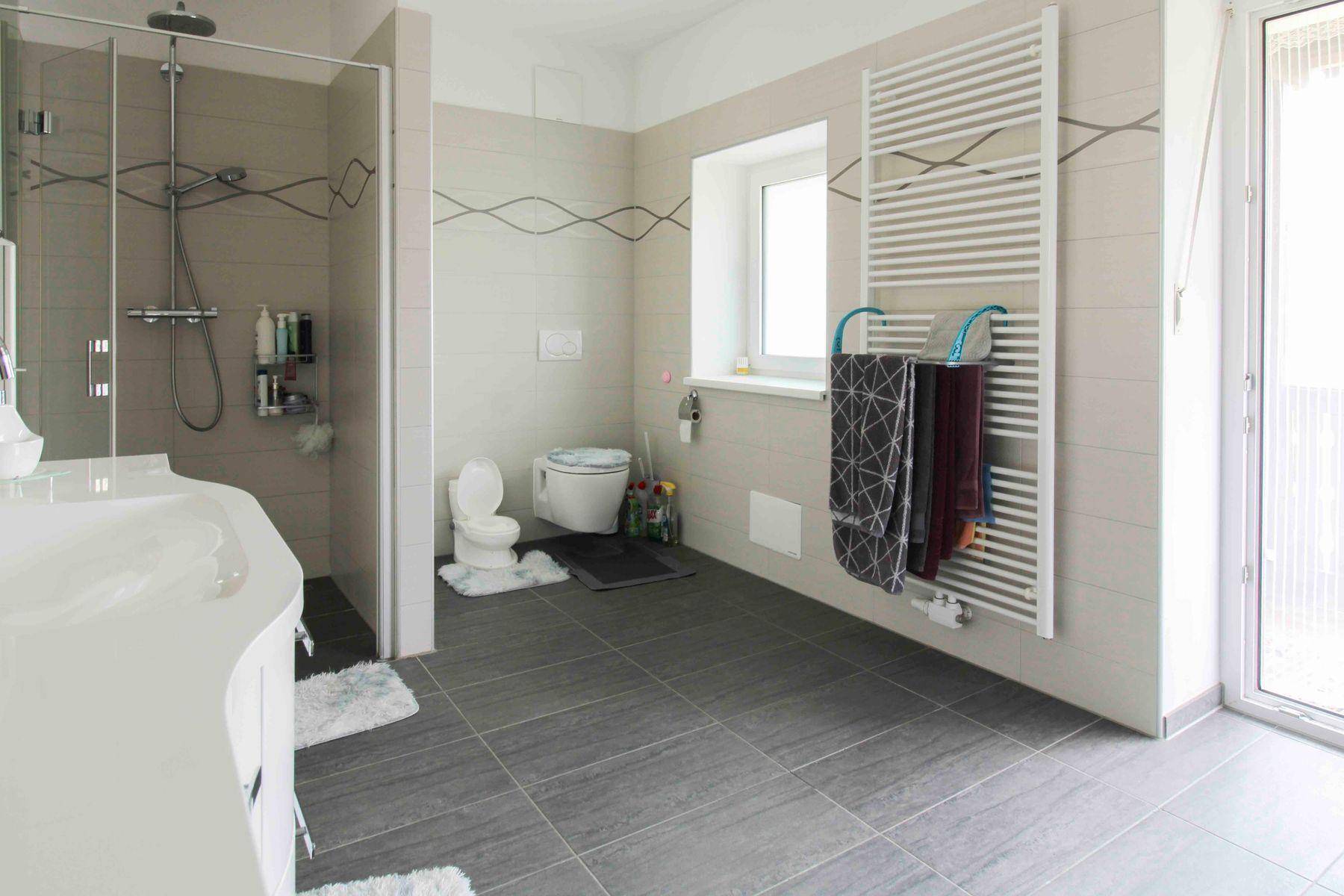 Modernes Badezimmer mit großer Duschkabine, Wand-WC und beheiztem Handtuchhalter, stilvoll gefliest.