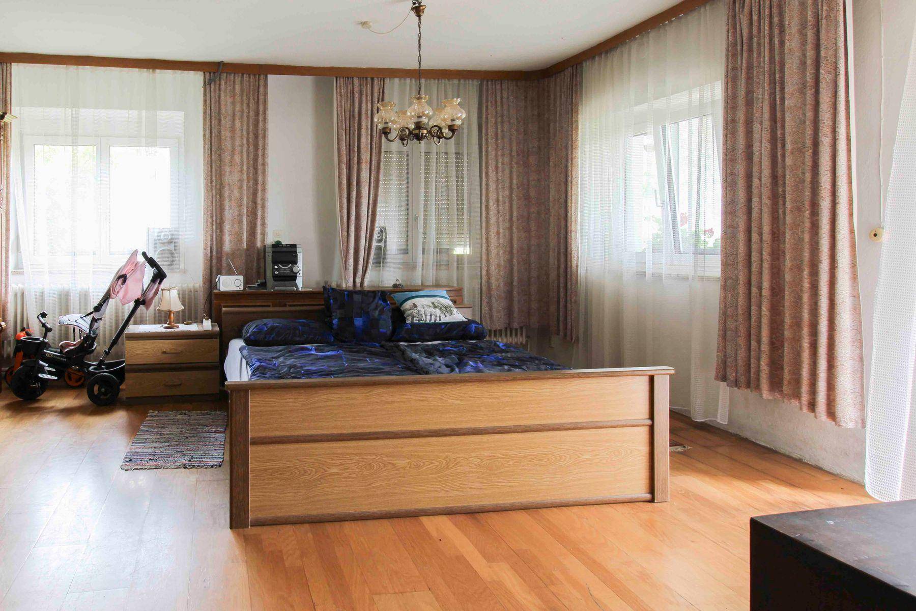 Geräumiges Schlafzimmer mit hellem Holzparkett, großem Bett und zwei Fenstern für viel Tageslicht.