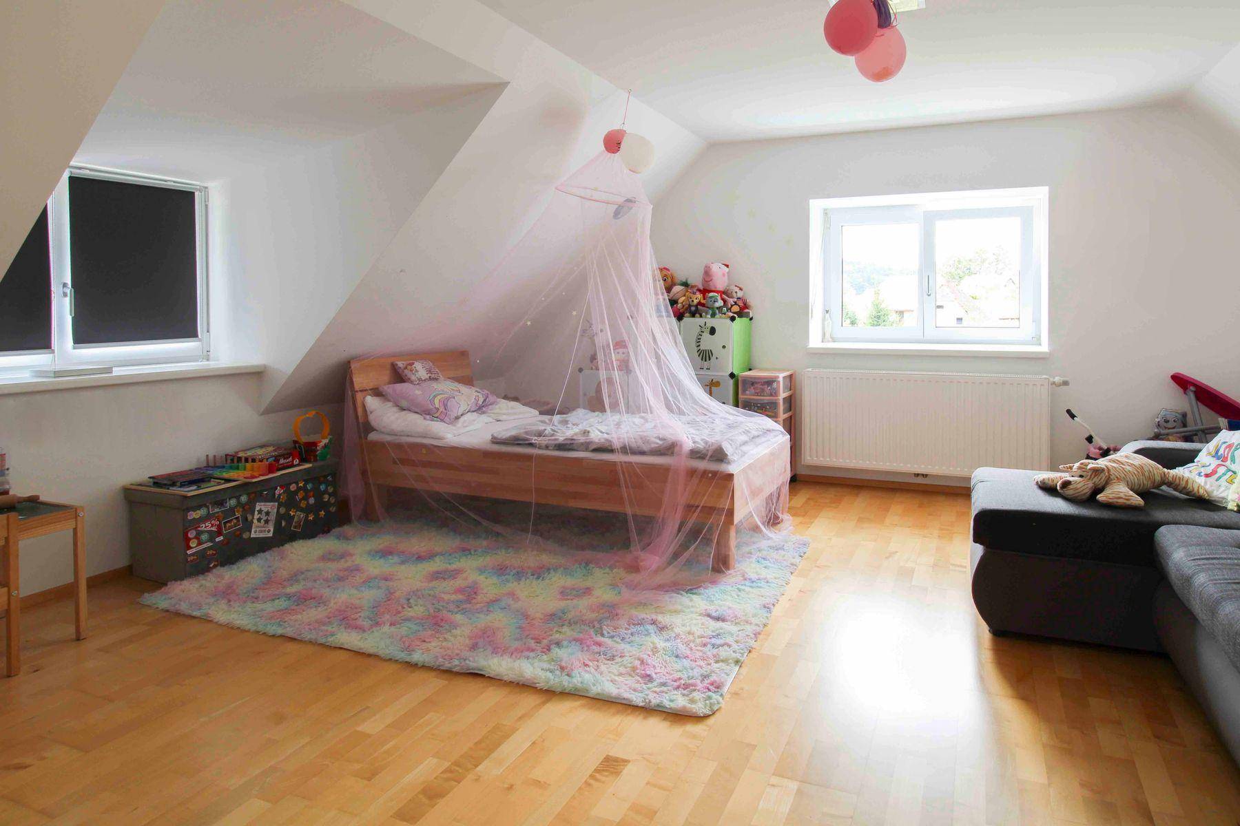Kinderzimmer im Dachgeschoss mit Holzparkett, Bett mit Himmel und bunter, freundlicher Dekoration.