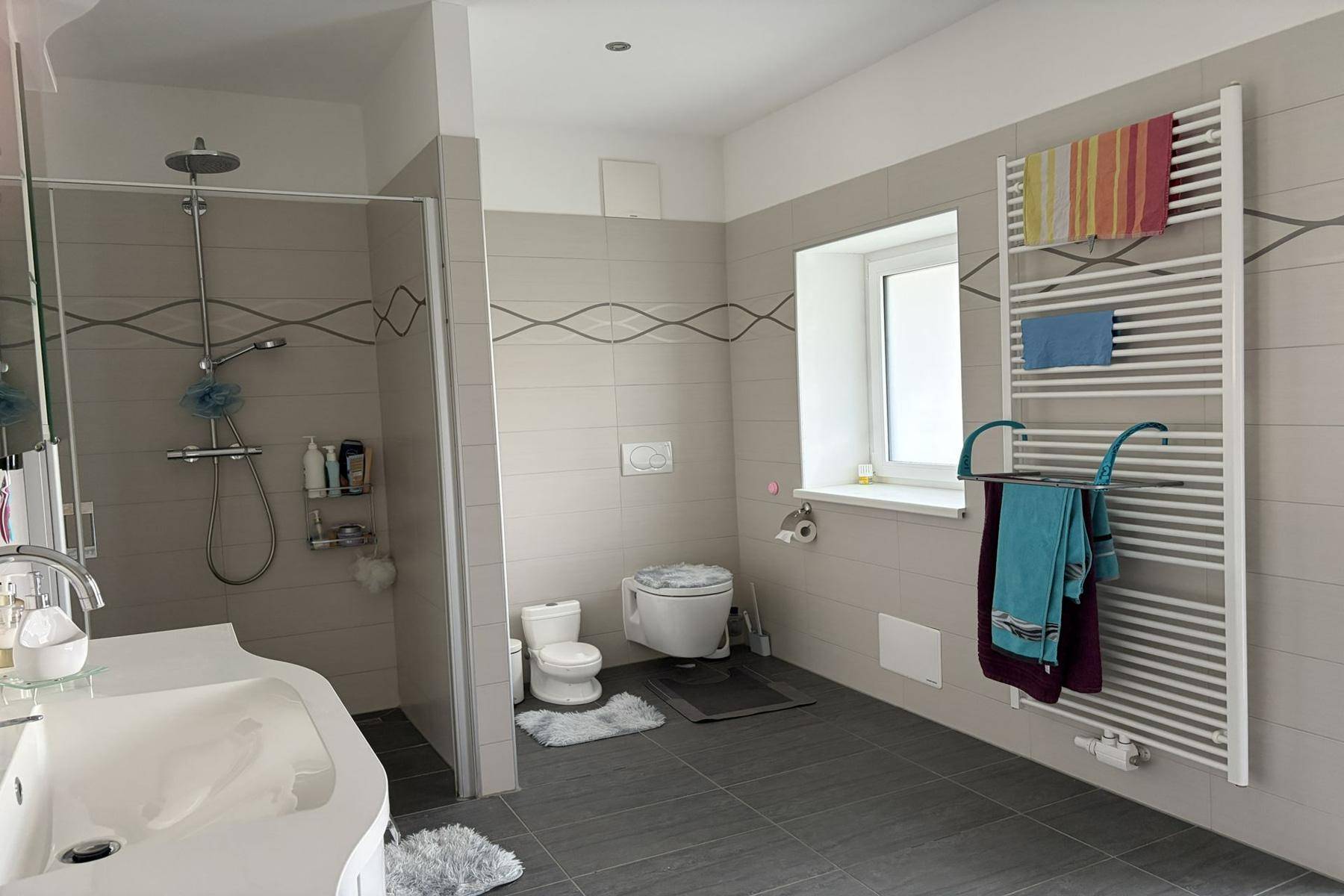 Modernes Badezimmer mit Duschkabine, Wand-WC, Einzelwaschbecken und beheiztem Handtuchhalter.