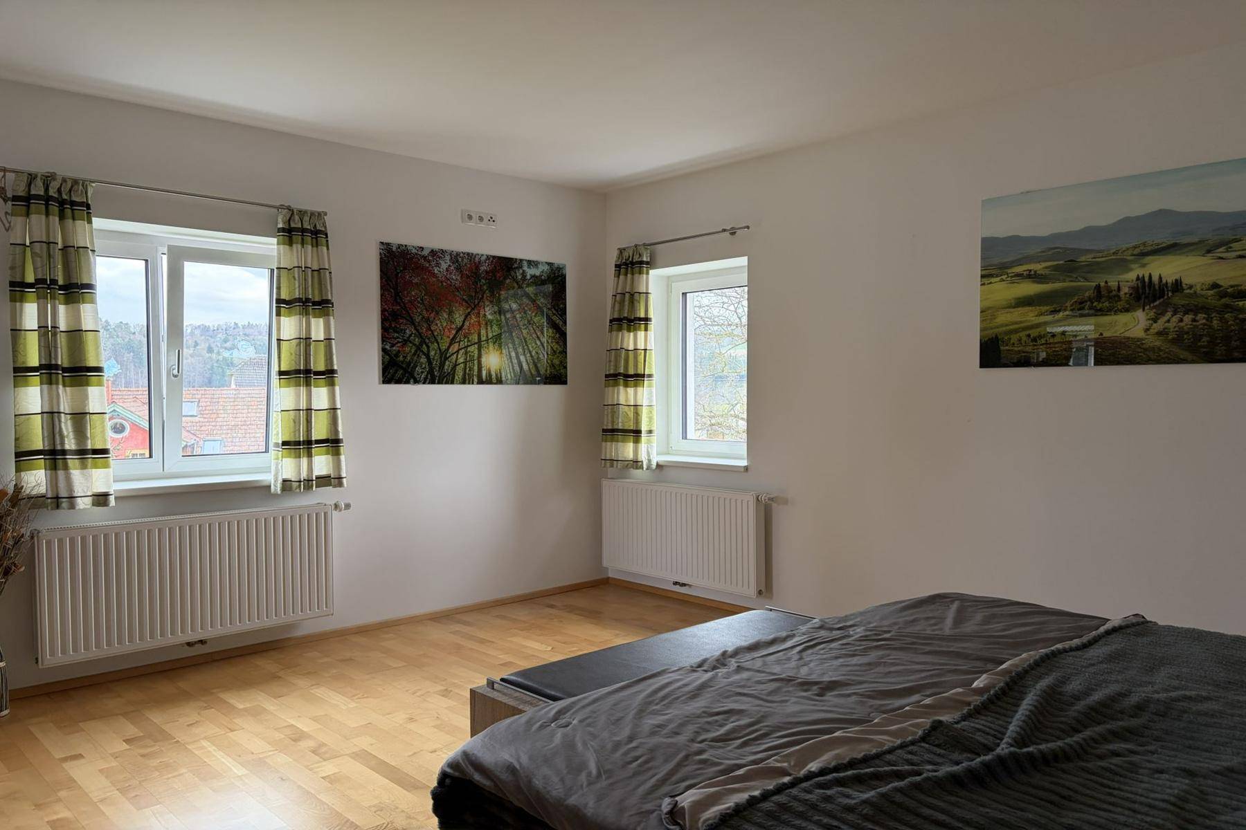 Helles Schlafzimmer mit Holzparkett, zwei Fenstern und moderner Wanddekoration, einladend und geräumig.