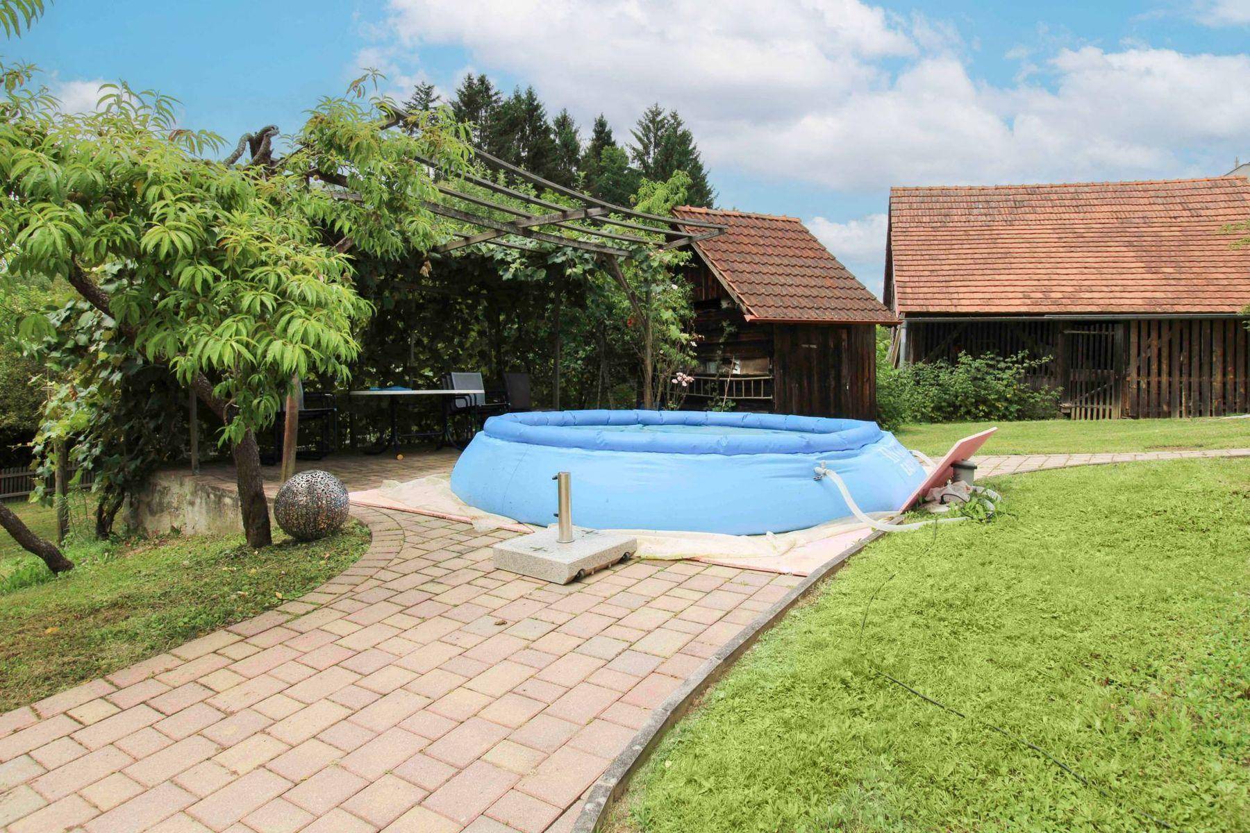 Gartenbereich mit aufblasbarem Pool, gepflastertem Weg und schattiger Sitzgelegenheit unter einer Pergola.