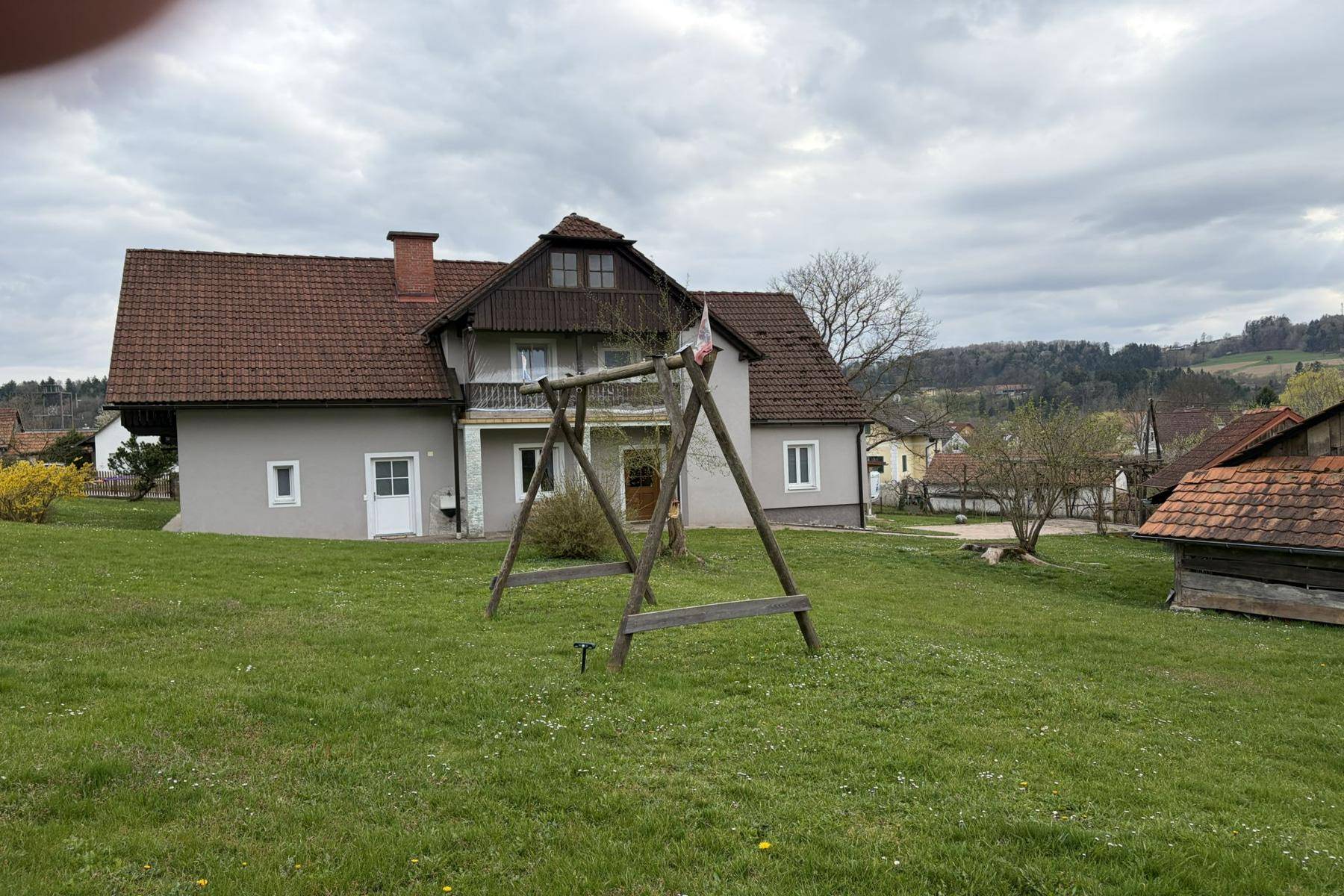Einfamilienhaus mit großem Garten, weitläufiger Rasenfläche und einer Holzschaukel im Vordergrund.