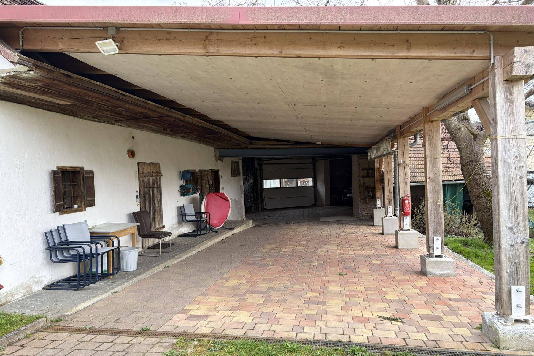 Geräumiger überdachter Bereich mit gepflastertem Boden, ideal als Carport oder Lagerfläche am Haus.