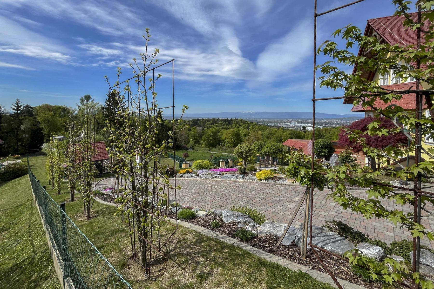 Eine gepflasterte Fläche im Garten mit Blumenbeeten und einem weiten Blick über die Landschaft.