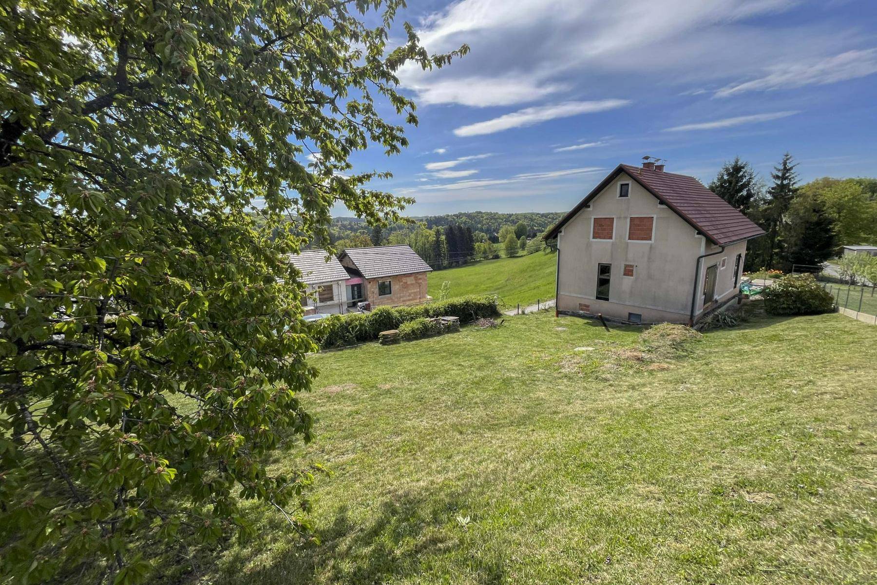 Zwei Häuser, eines im Bau, stehen auf einem grünen Hügel mit weitem Blick über die Landschaft.
