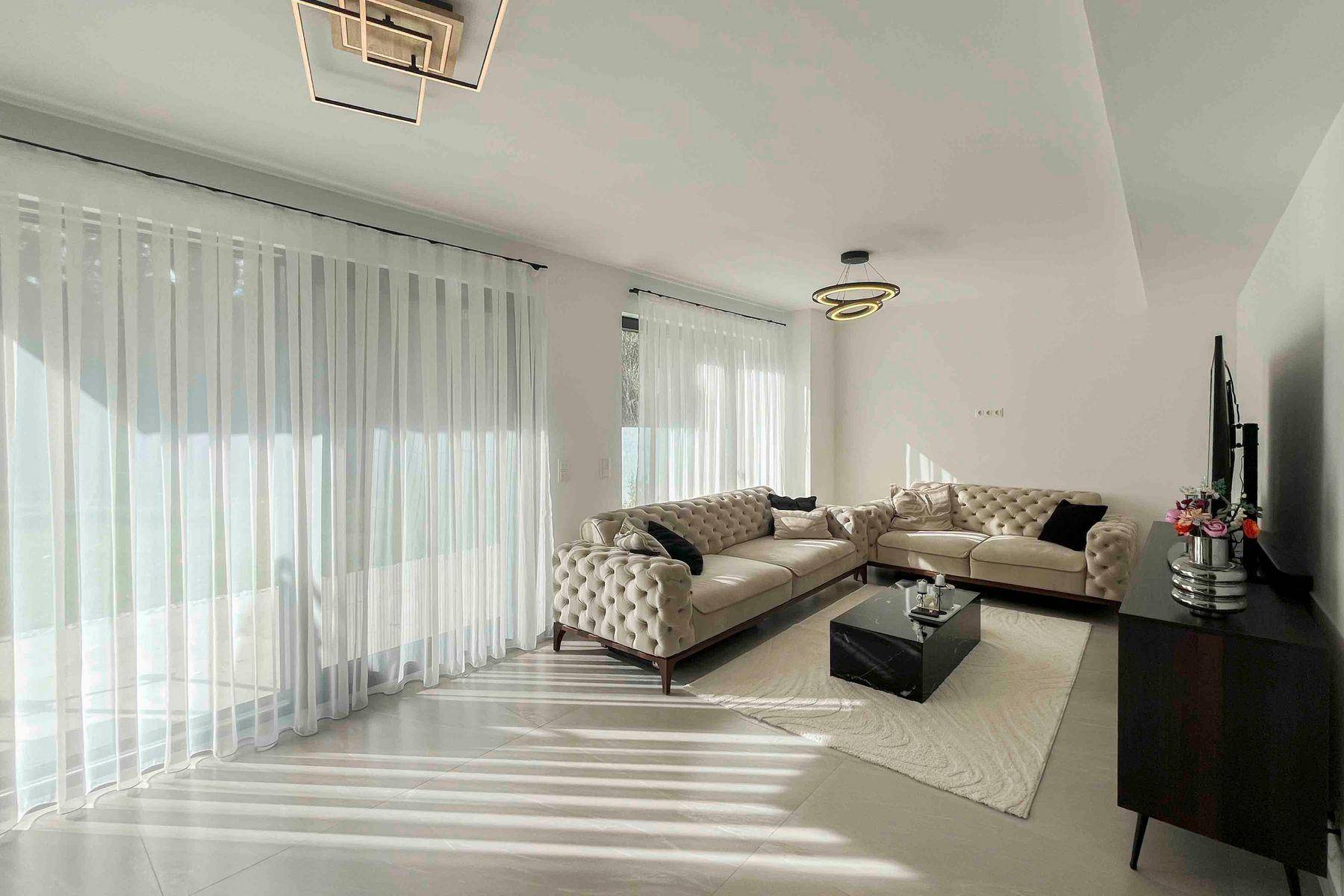 Helles Wohnzimmer mit modernen Sofas, großformatigen Fliesen und großen Fenstern.