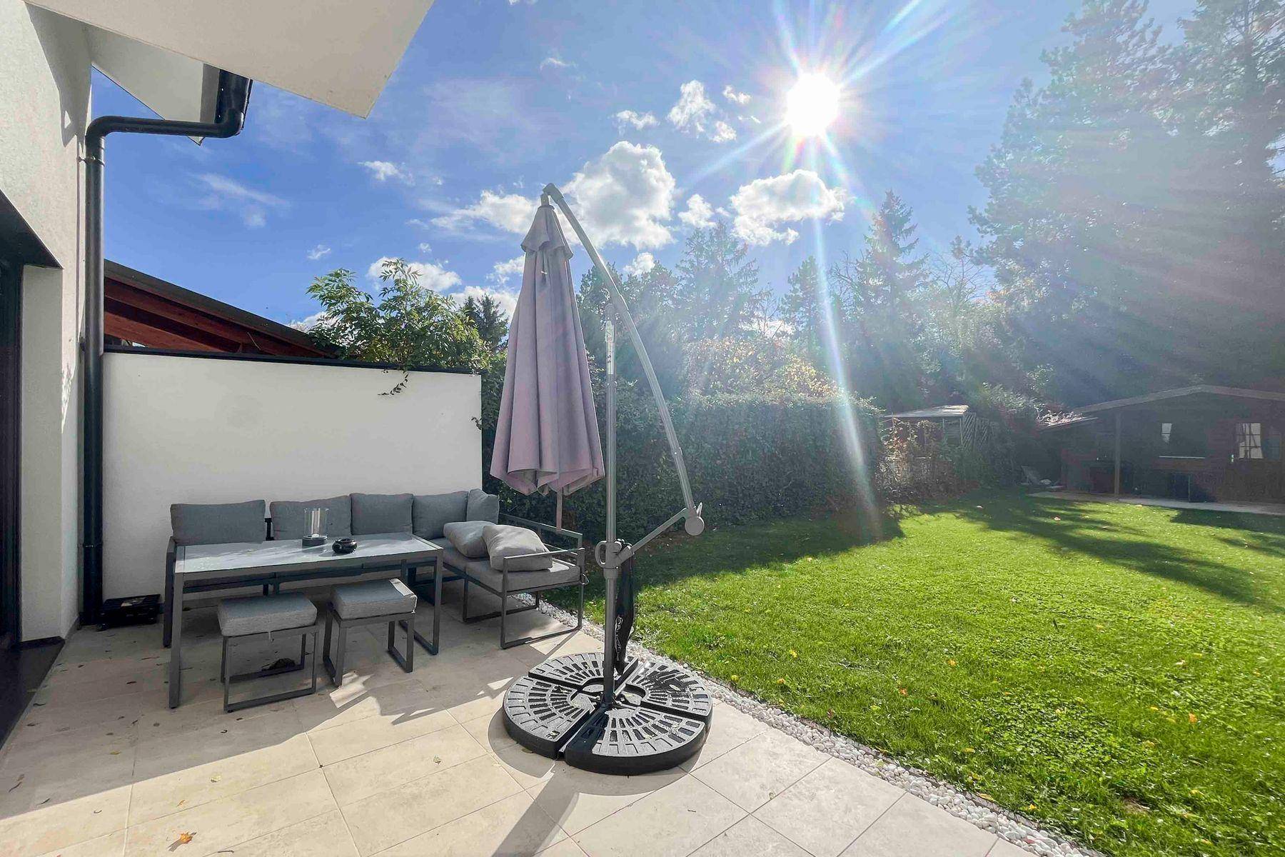 Gemütliche Terrasse mit modernen Gartenmöbeln und großem Sonnenschirm im Grünen.
