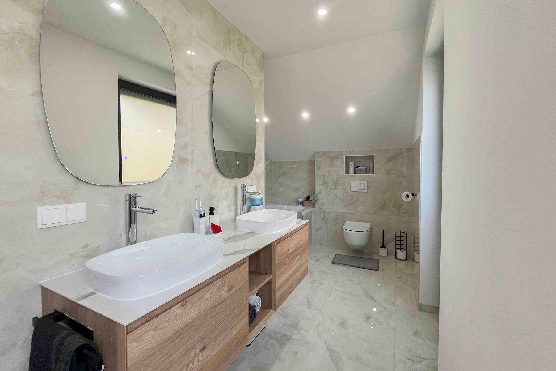 Großes modernes Badezimmer mit Doppelwaschbecken, Wand-WC und eleganten Fliesen.