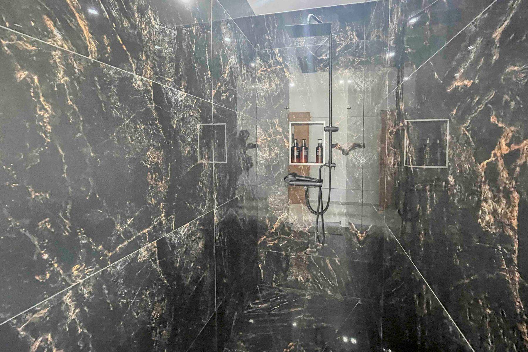 Elegante Dusche mit schwarzen Marmorfliesen und moderner Regendusche.
