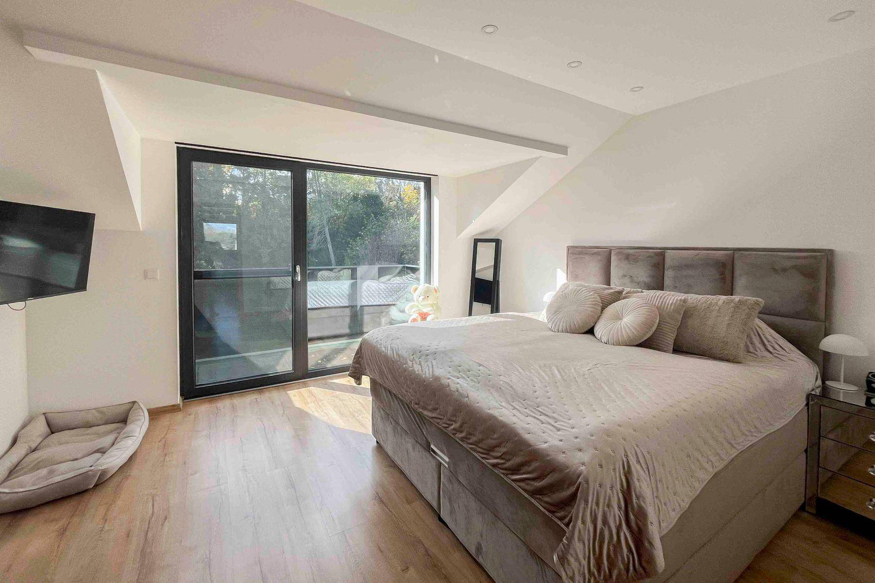 Geräumiges Schlafzimmer mit großem Bett, Holzboden und Zugang zu einem Balkon.