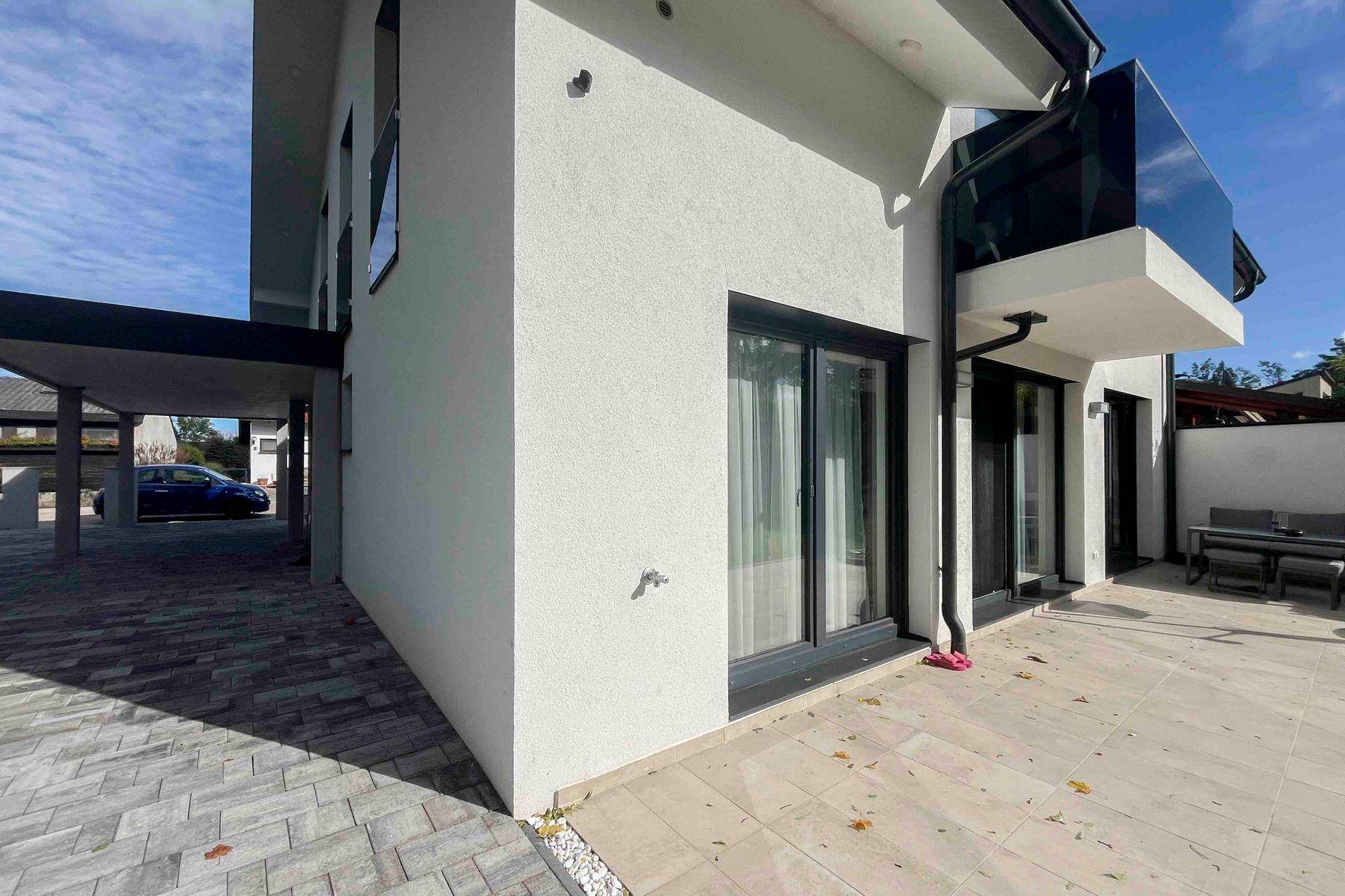 Seitenansicht des Hauses mit gepflasterter Terrasse, Carport und Zufahrt.