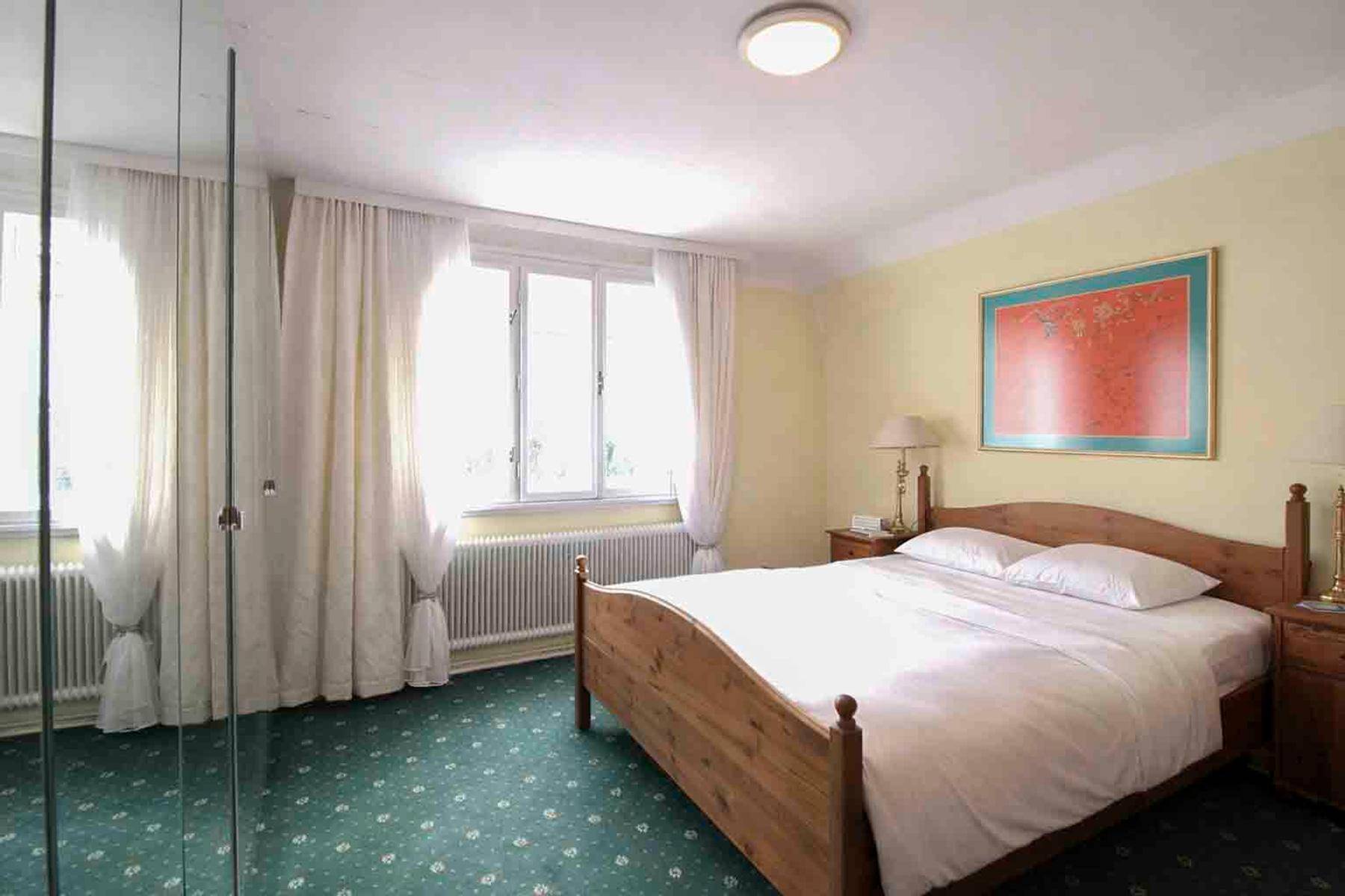 Schlafzimmer mit Holzbett, grüner Teppichboden und großen Fenstern.