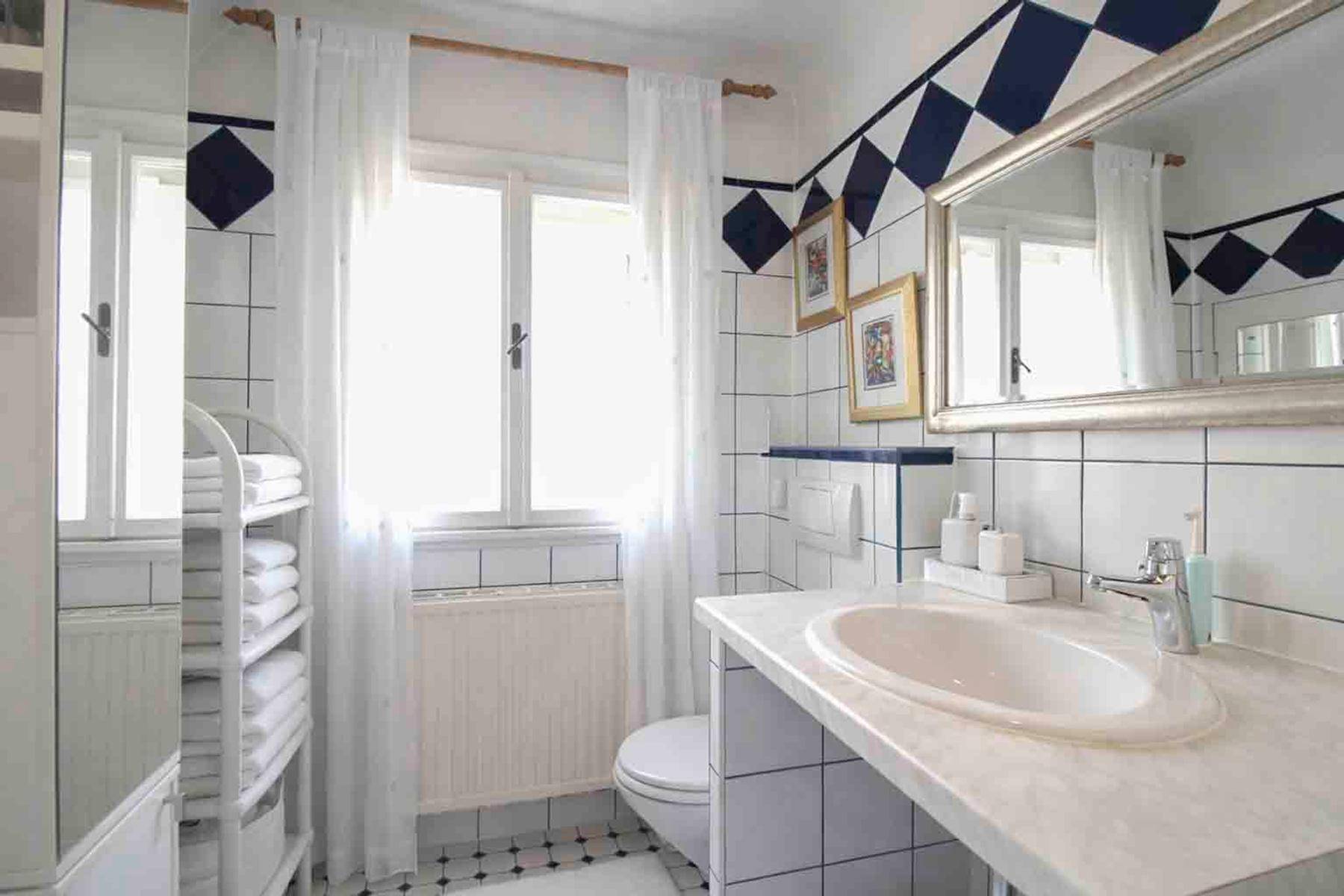Badezimmer mit Fliesen, Waschbecken, Toilette und einem Fenster.