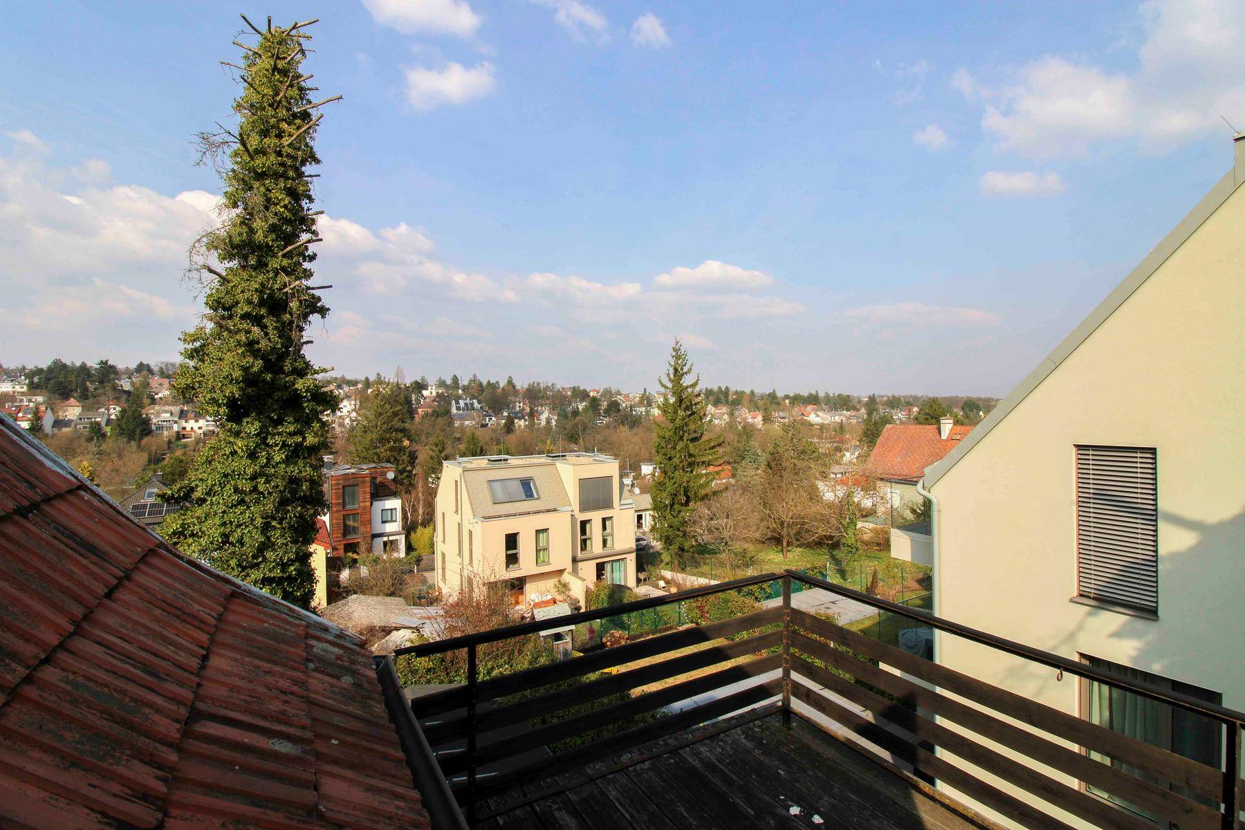 Alter Holzbalkon mit Blick auf die umliegende Wohngegend und grüne Bäume.