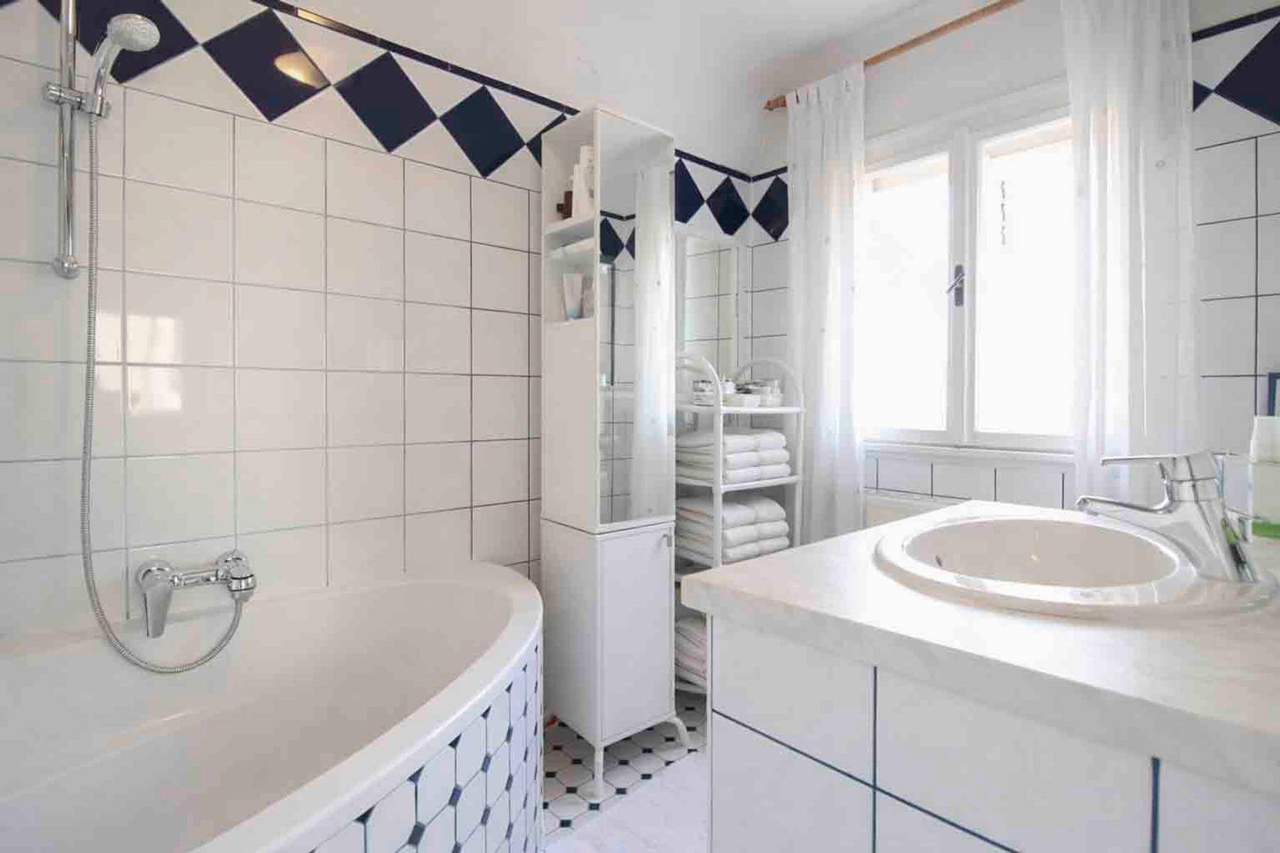 Badezimmer mit Badewanne, Waschbecken und Fliesen in Weiß und Blau.