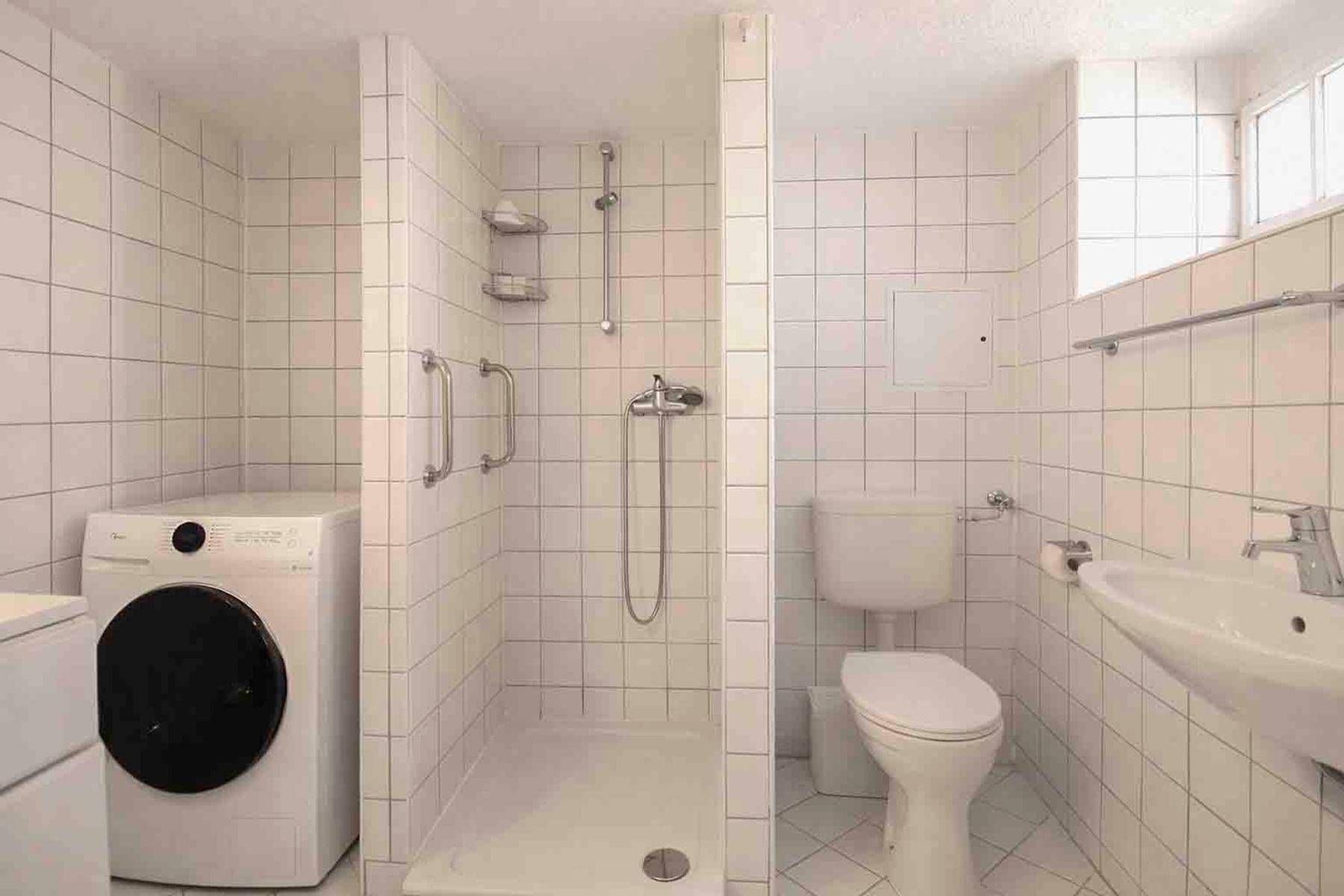 Funktionales Badezimmer mit Dusche, Toilette, Waschbecken und Waschmaschine.