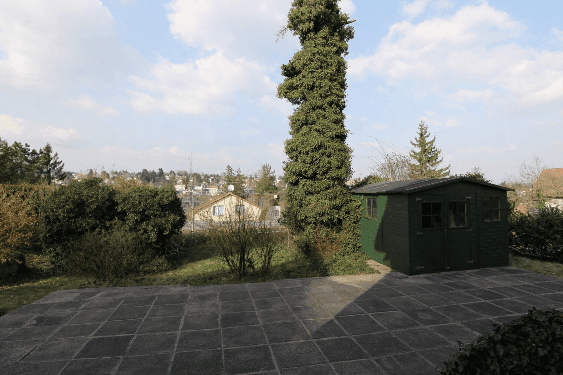 Gepflasterte Terrasse mit Gartenhaus und Blick auf die Umgebung.