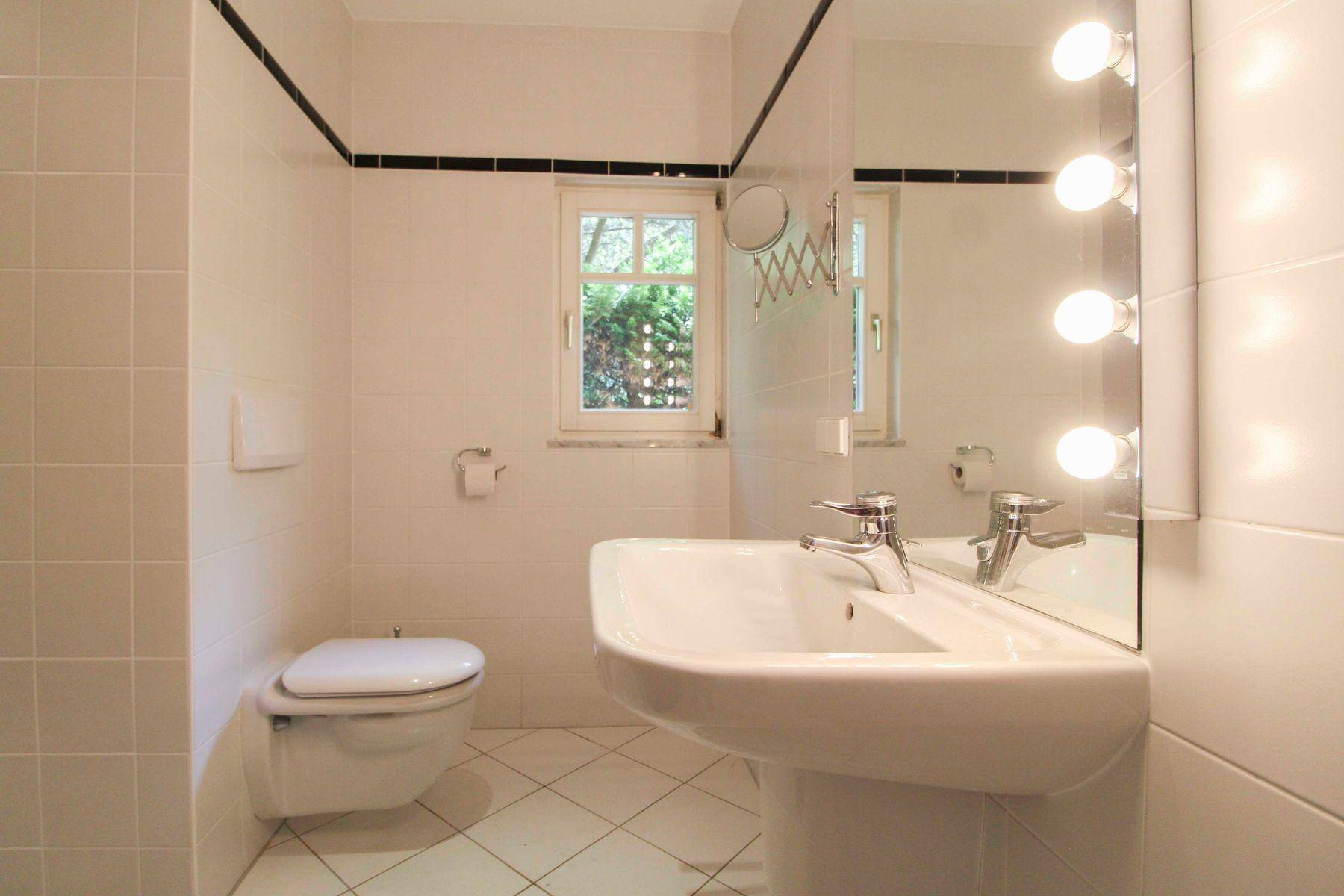 Helles Badezimmer mit weißen Fliesen, Standwaschbecken, wandhängendem WC und Fenster.