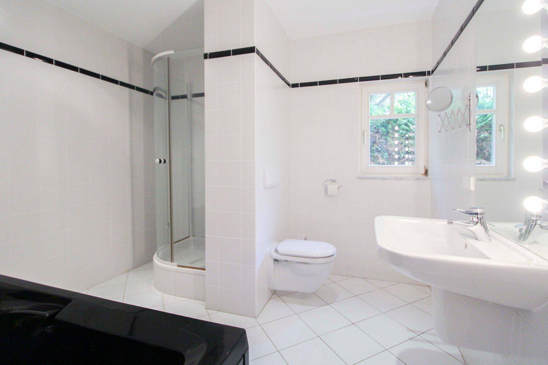 Badezimmer mit Duschkabine, weißen Fliesen, Standwaschbecken und wandhängendem WC.