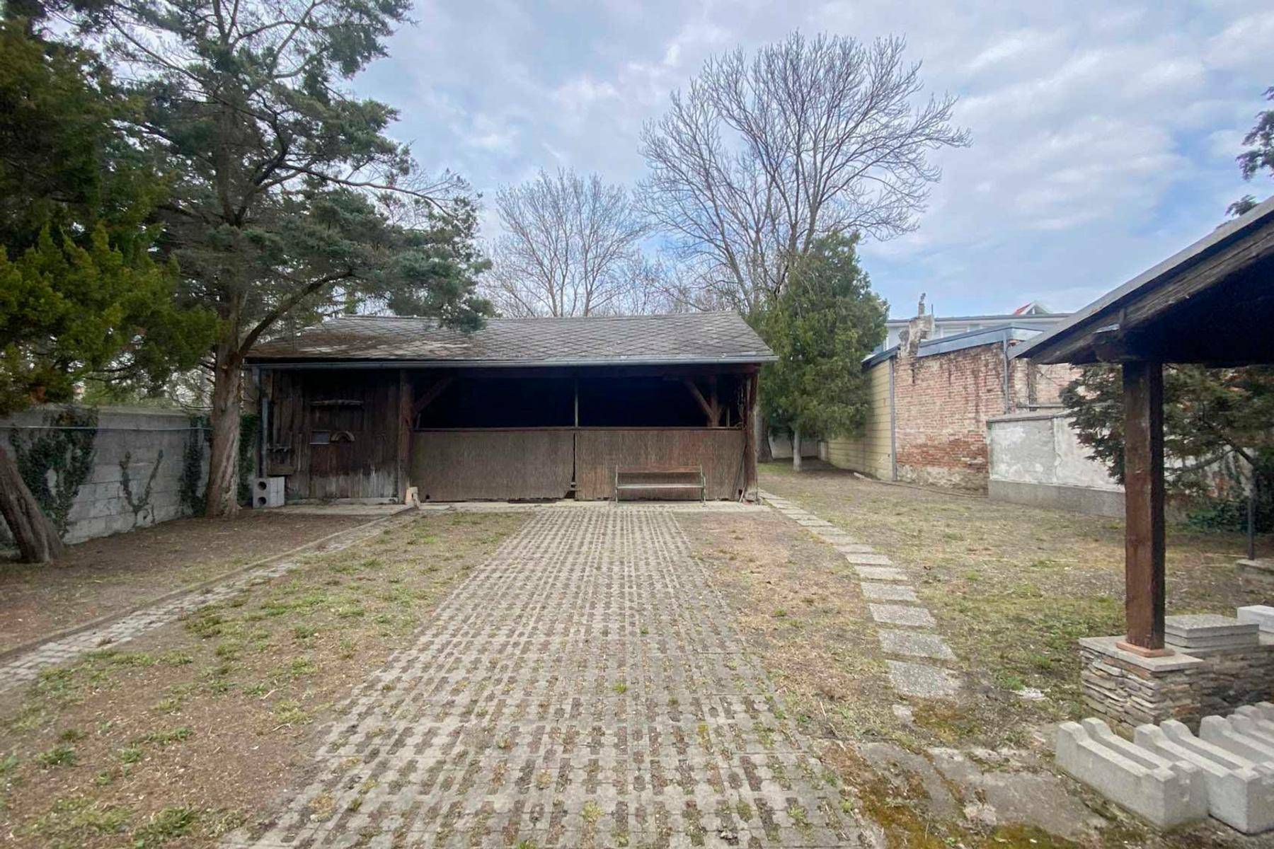 Außenbereich mit einem Holzschuppen oder Carport und einem gepflasterten Weg im Garten.