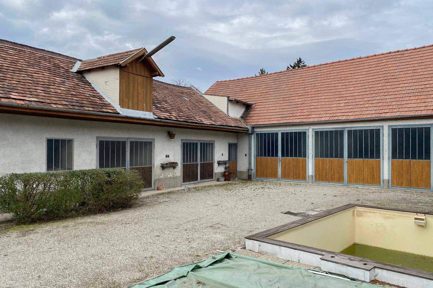 Gesamtanblick des Anwesens mit mehreren Gebäuden und einem ungenutzten Pool im Vordergrund.