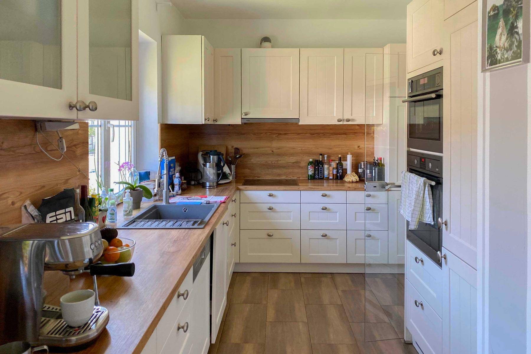Moderne Einbauküche mit weißen Schränken, Holz-Arbeitsplatten und integrierten Geräten, bietet viel Stauraum.