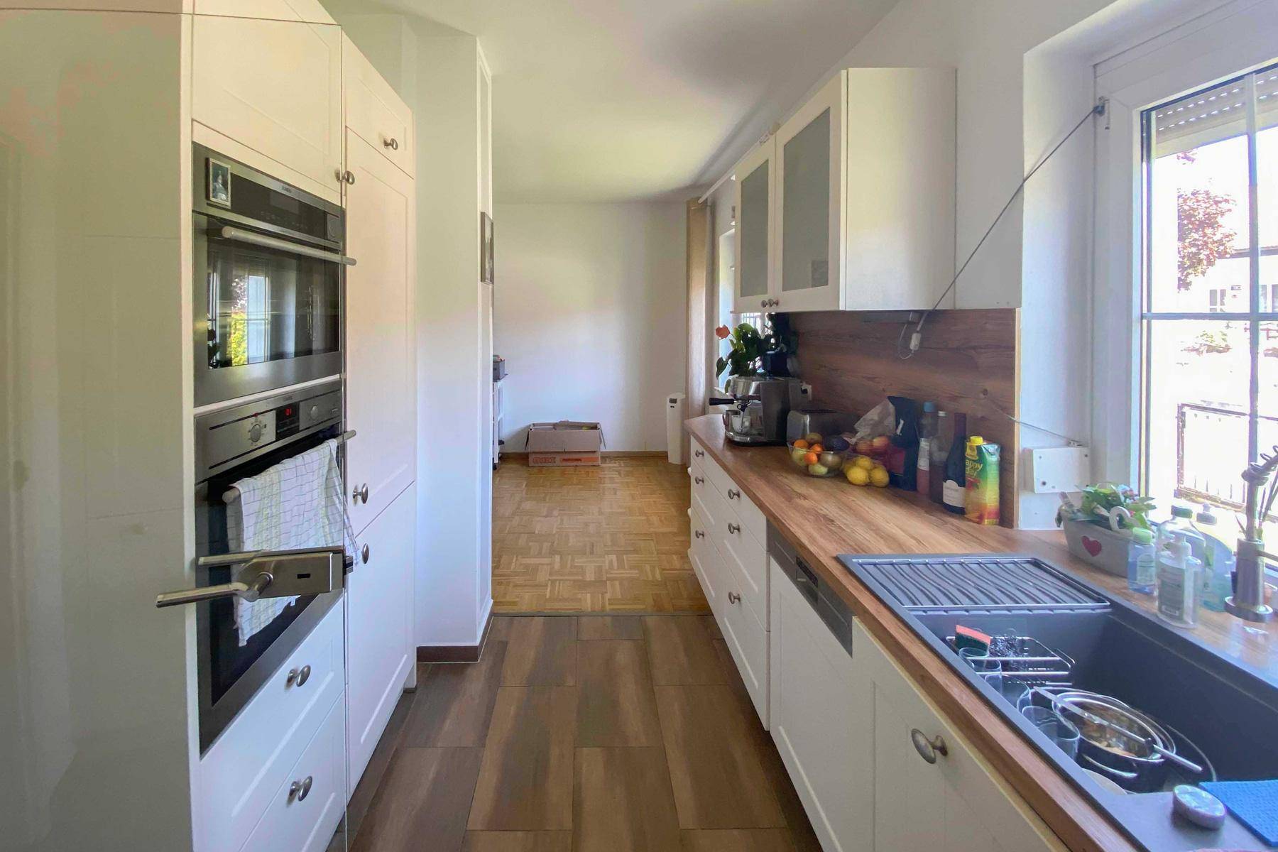 Funktionale Küche mit weißen Schränken und Holz-Arbeitsplatten, gut beleuchtet durch ein großes Fenster.