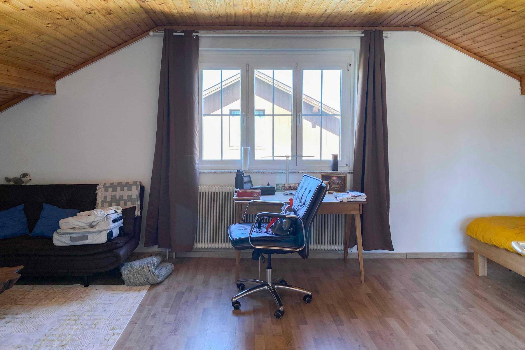Gemütliches Dachzimmer mit Holzdecke und Schreibtisch, ideal als Arbeits- oder Gästezimmer mit viel Tageslicht.