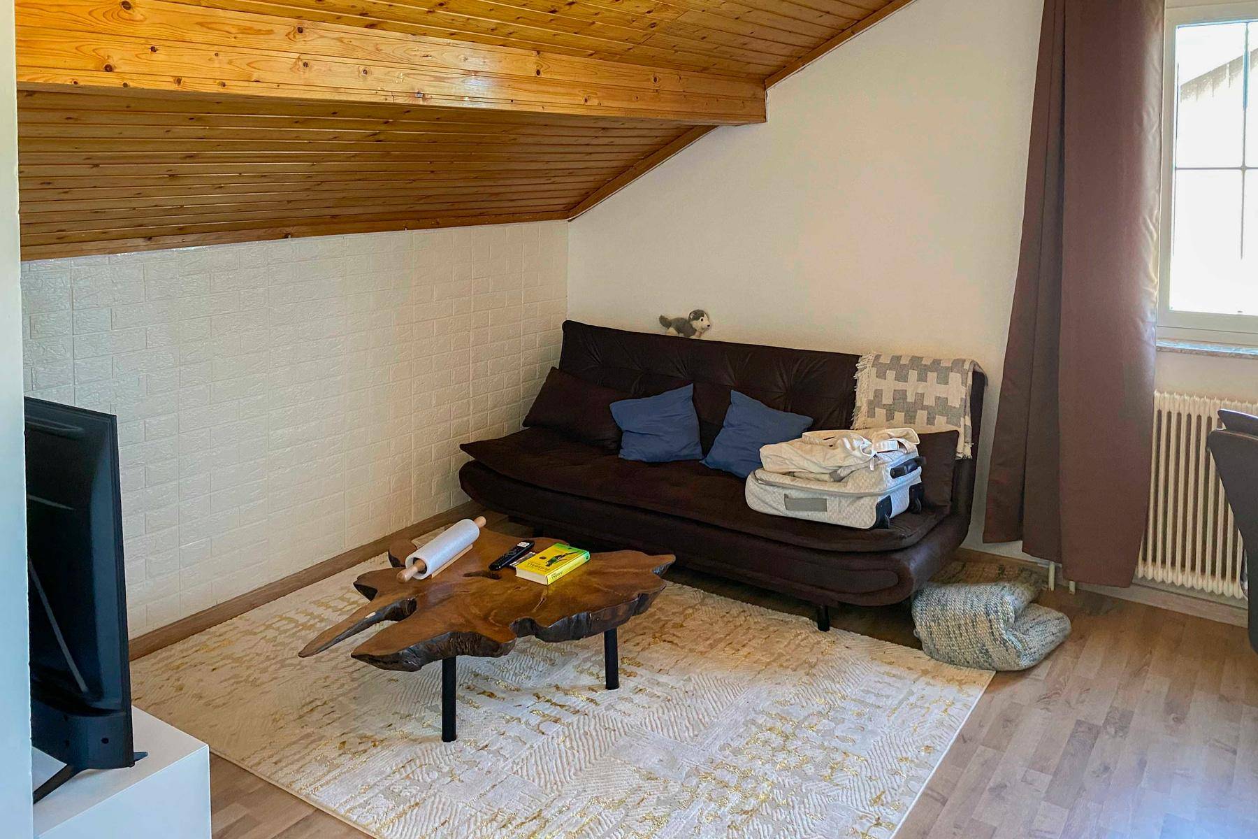 Gemütlicher Wohnbereich im Dachgeschoss mit Holzbalkendecke, Sofa und einem einzigartigen Holztisch.