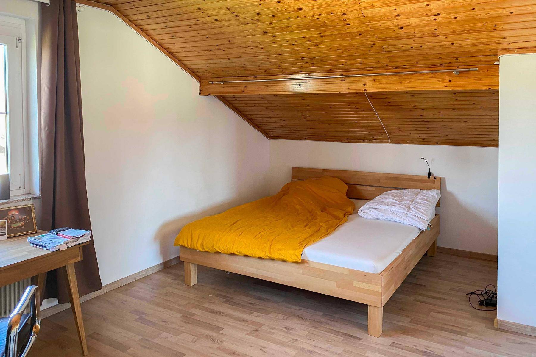 Helles Schlafzimmer im Dachgeschoss mit Holzbalkendecke und Holzboden, bietet eine warme und einladende Atmosphäre.