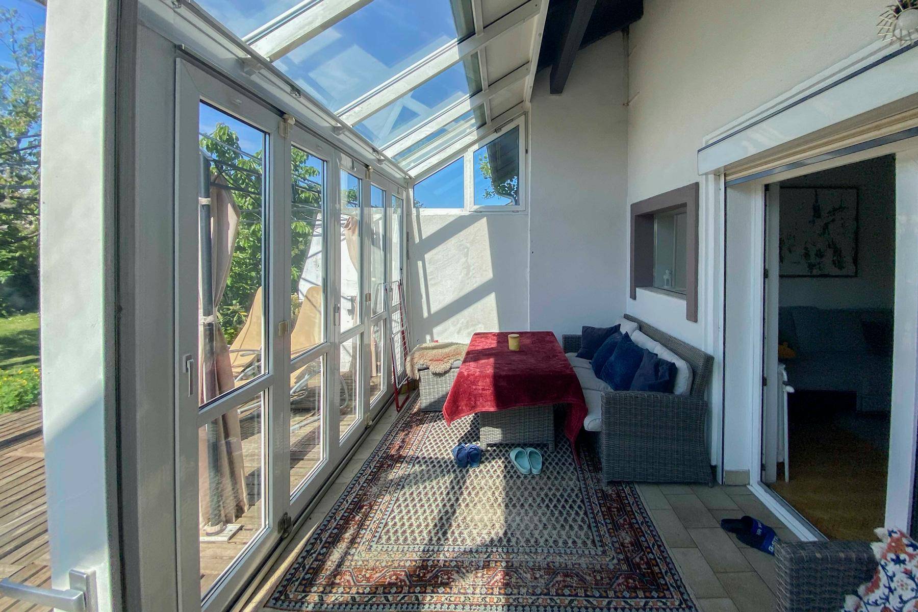 Heller Wintergarten mit Essbereich und direktem Zugang zur Holzterrasse, ideal für entspannte Stunden.